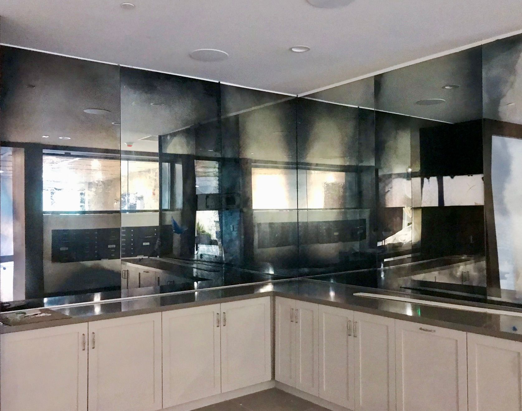 White kitchen cabinets under a wall of antiqued, dark-tinted mirror panels reflecting the room.