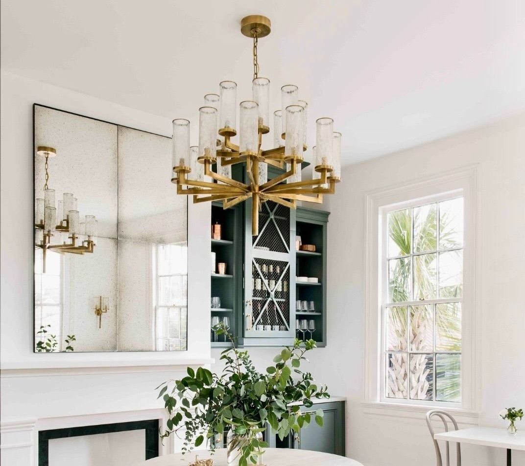 A dining room with a chandelier hanging from the ceiling and an antique mirror on the wall.