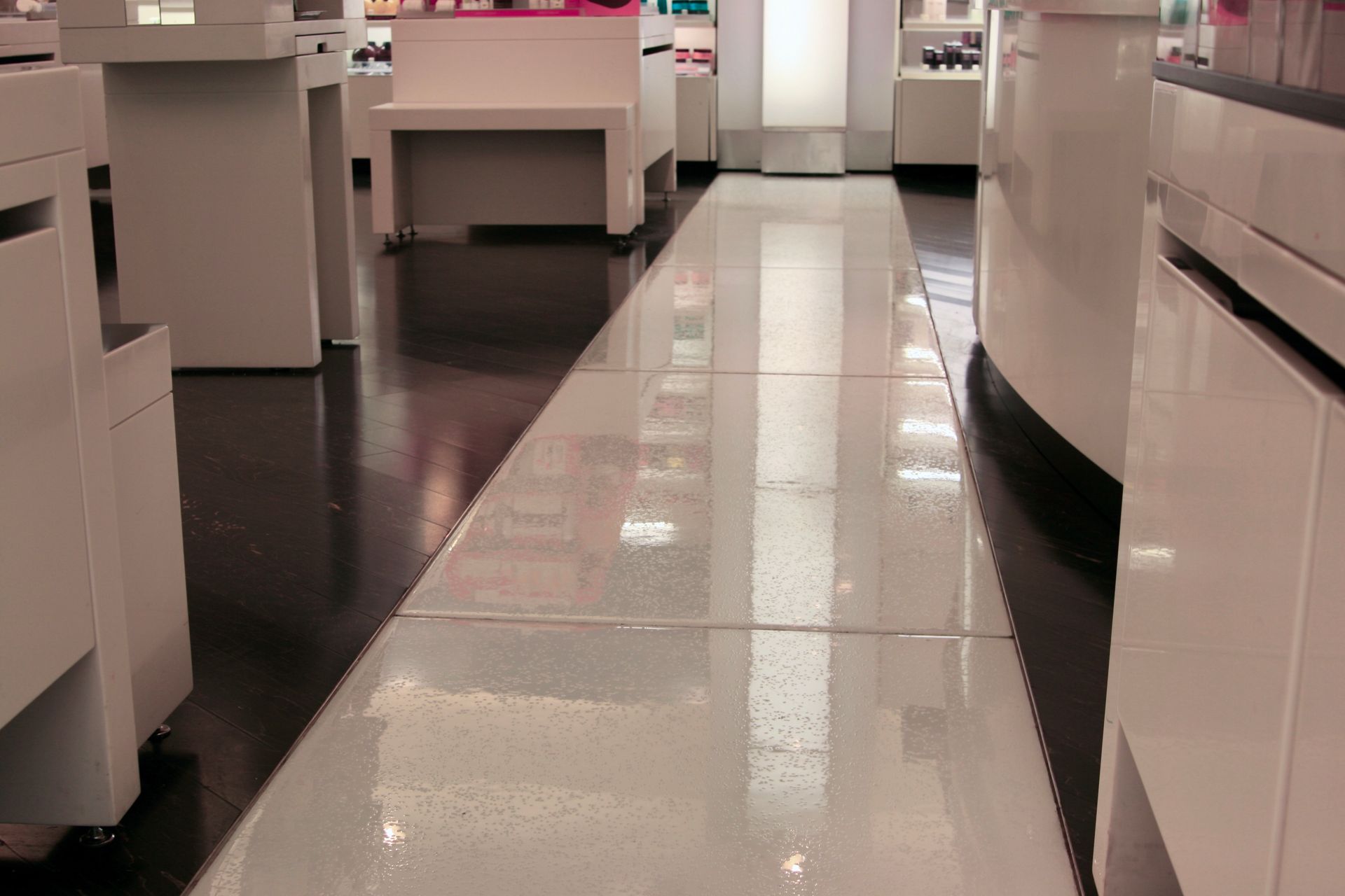 Glossy white glass floor in a store, reflecting white shelves and bright lights.