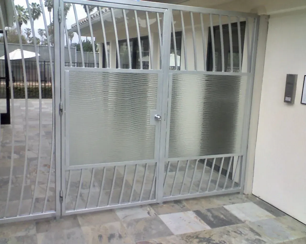 Gray metal security gate with textured cast glass panels and diagonal bars. Exterior view.