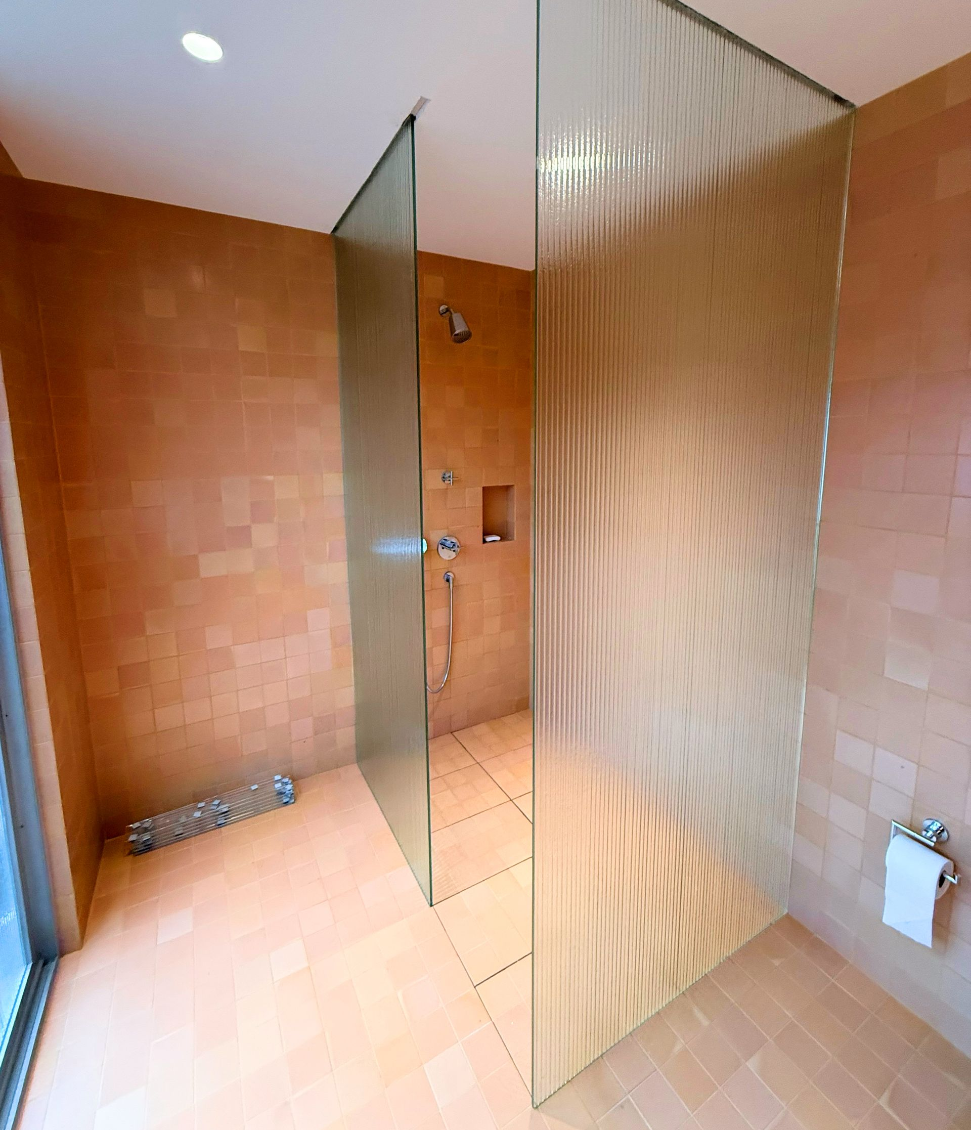 Shower with glass partitions, terracotta tile walls, and modern fixtures.