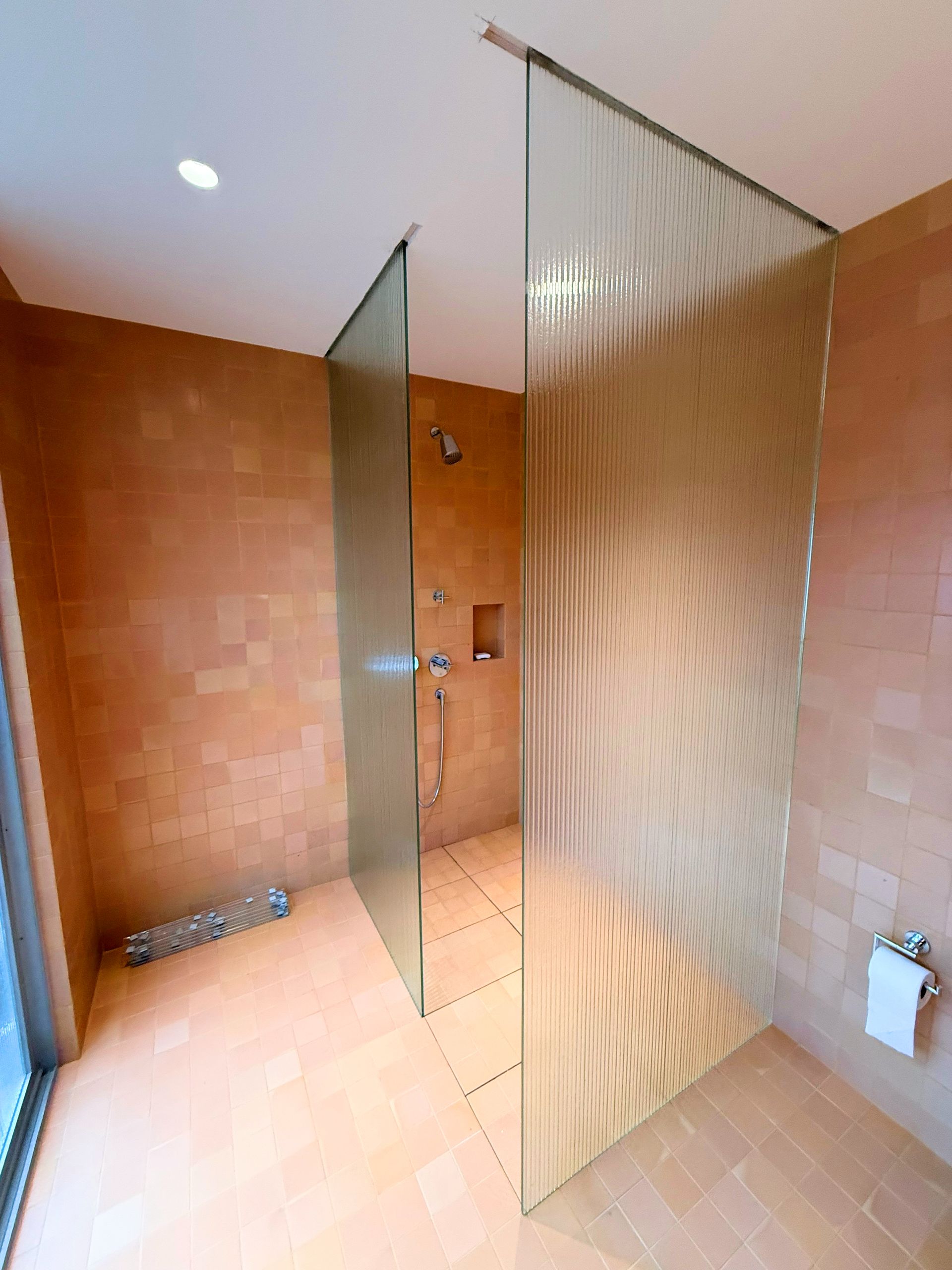 Modern shower stall with textured glass panels, beige tiled walls, and floors in a spacious bathroom.