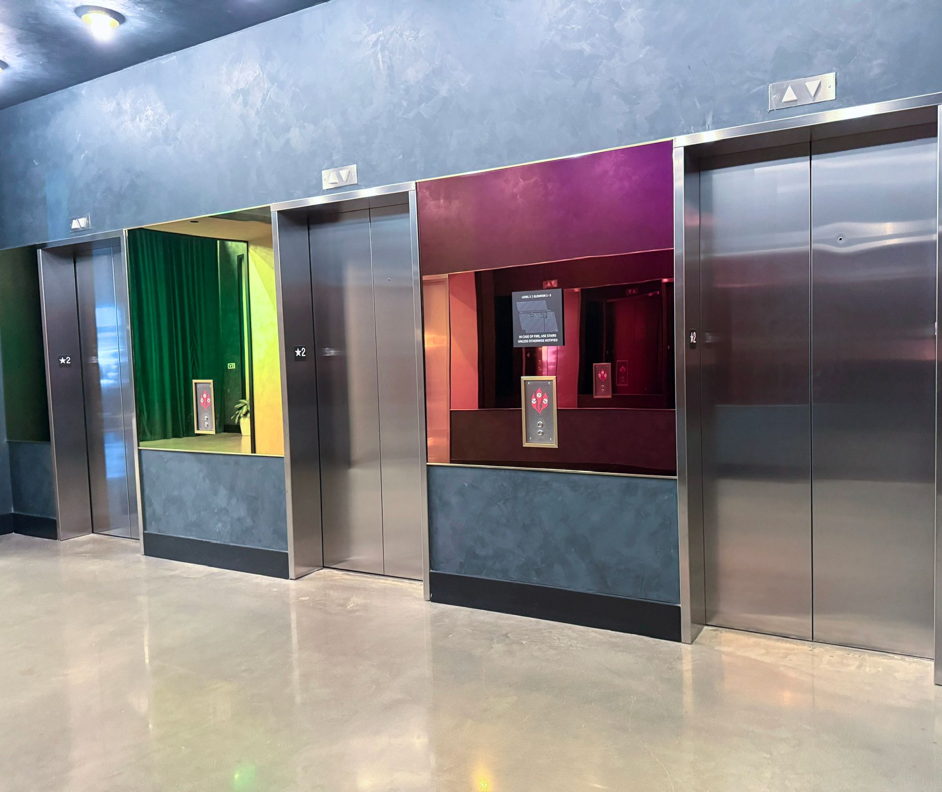 A row of stainless steel elevators in a building featuring peacock glass