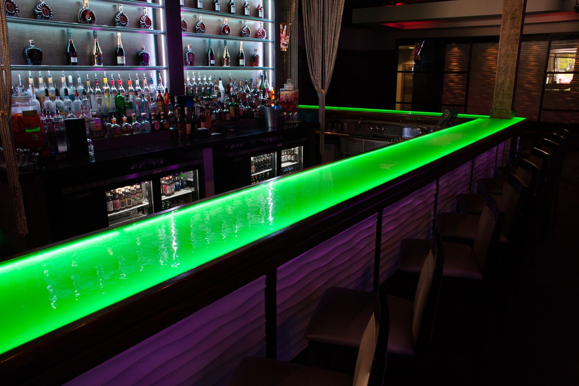 Glass countertop with integrated LED lights glowing a neon green at a bar.