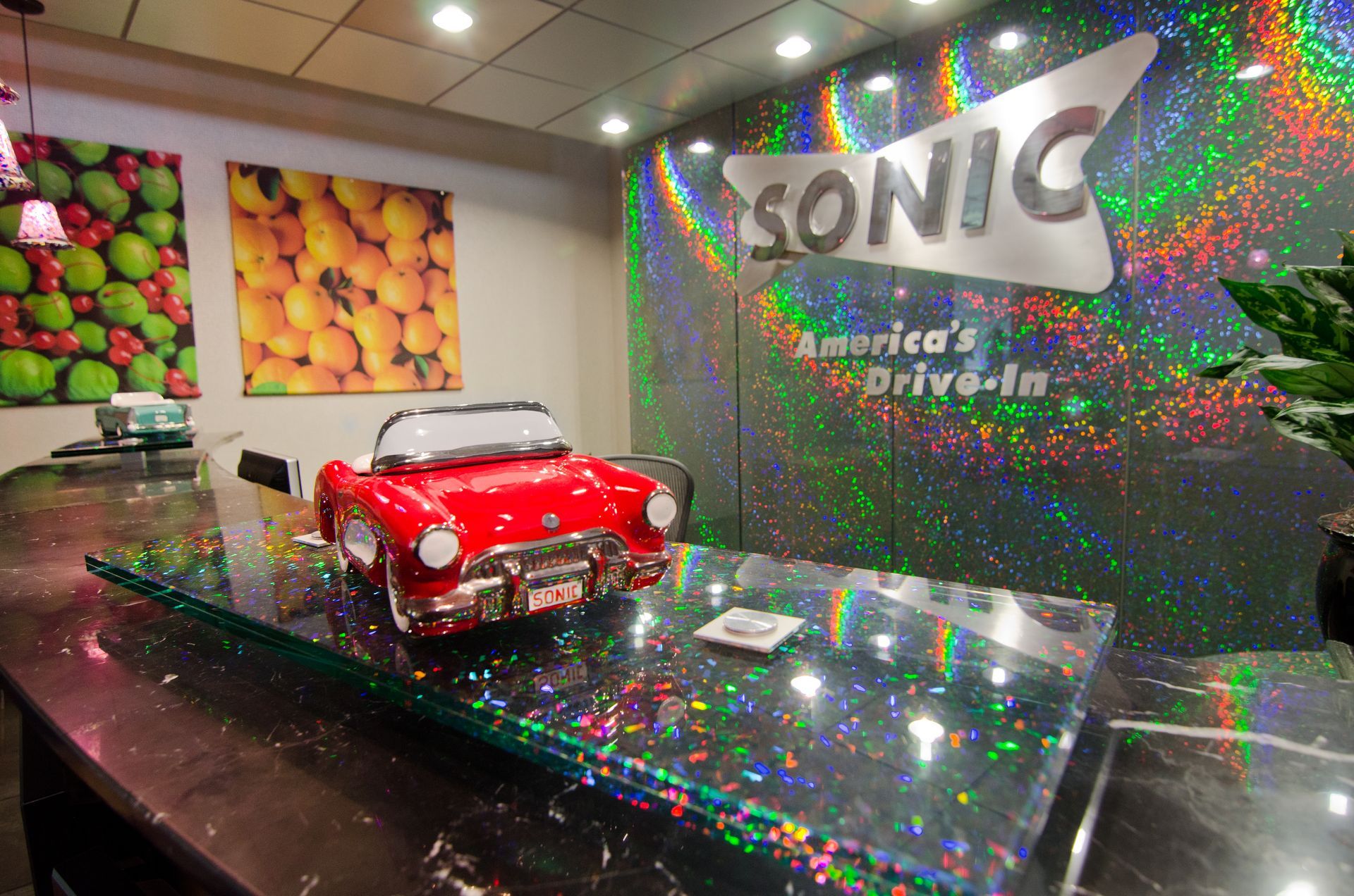 A toy car is sitting on a counter in front of a hologram glass sign that says sonic america 's drive-in