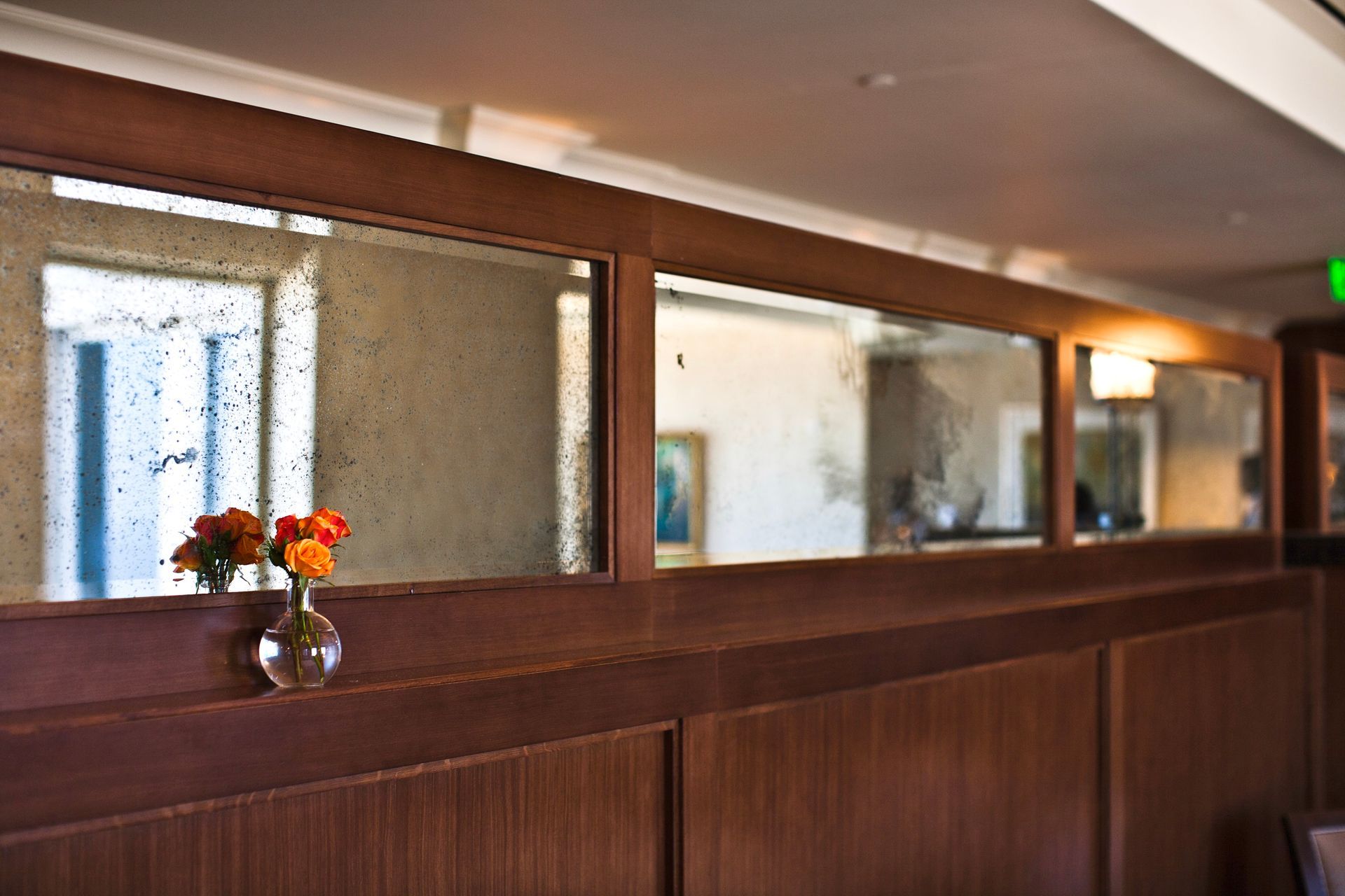 A vase of flowers sits on a wooden wall in front of an antique mirror.