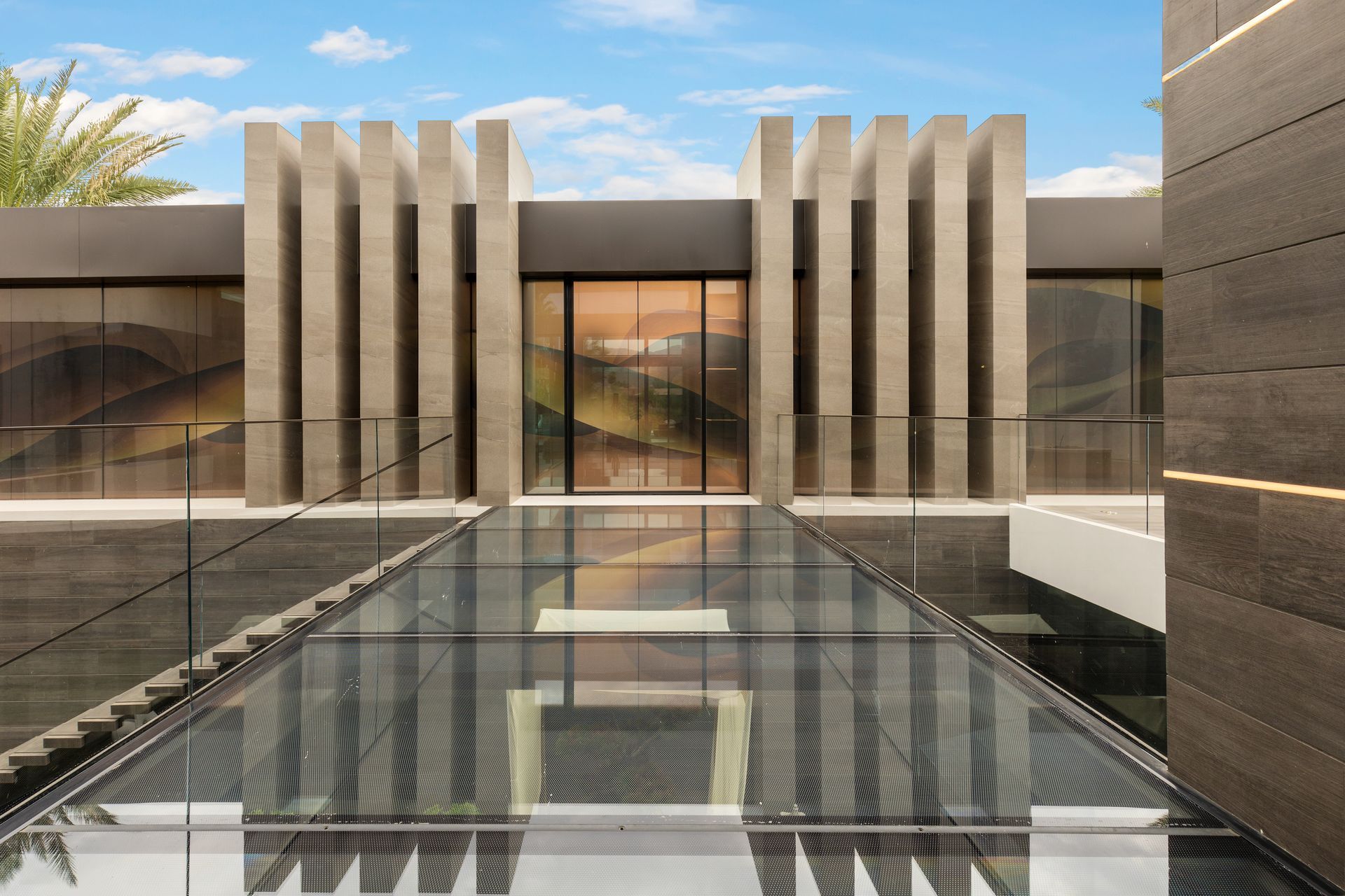 Modern building exterior with glass walkway, concrete pillars, and a water feature.