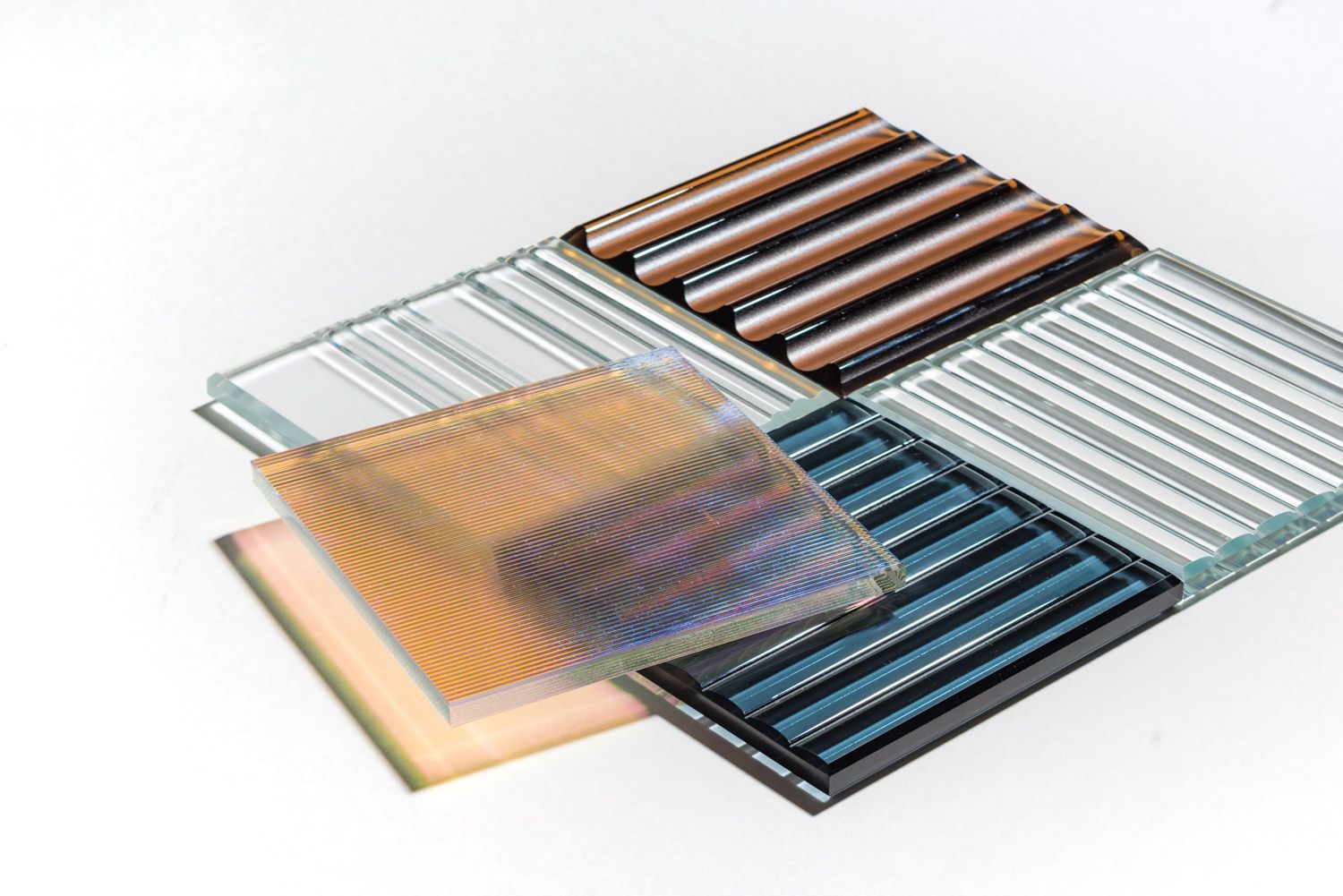 Assorted glass panels with textured surfaces, varying colors and patterns, arranged on a white surface.