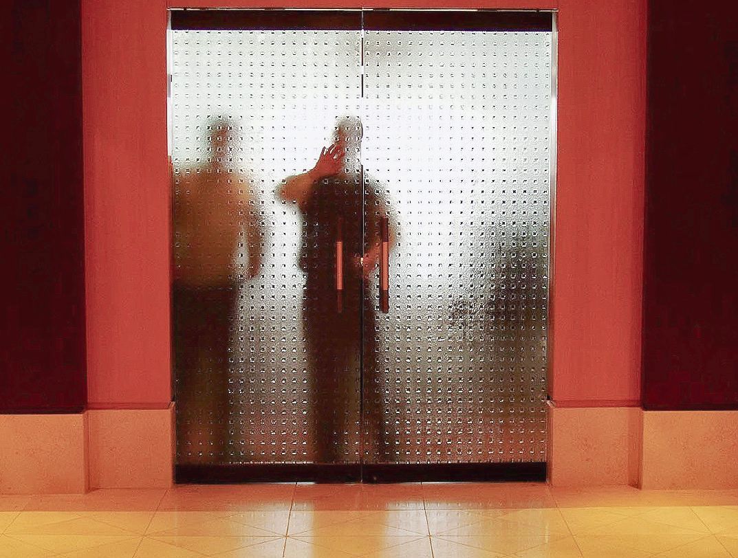 Silhouetted figures behind a textured glass panel, set between dark maroon walls and pale floor.