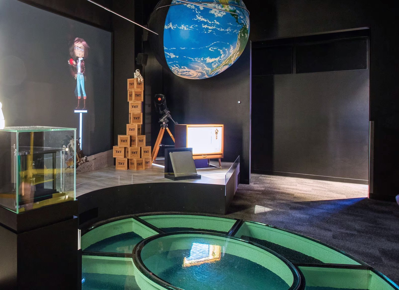 An art installation with a large globe, water feature, digital display, and a figure on a pedestal.