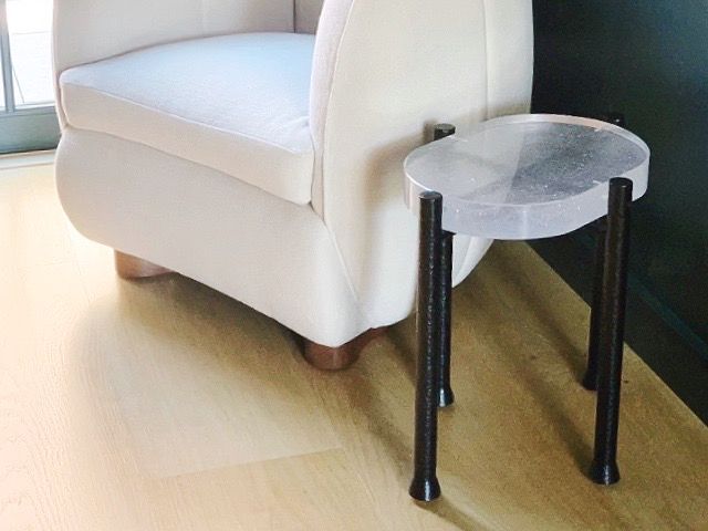 A small table with a glass table top is sitting next to a chair on a wooden floor.