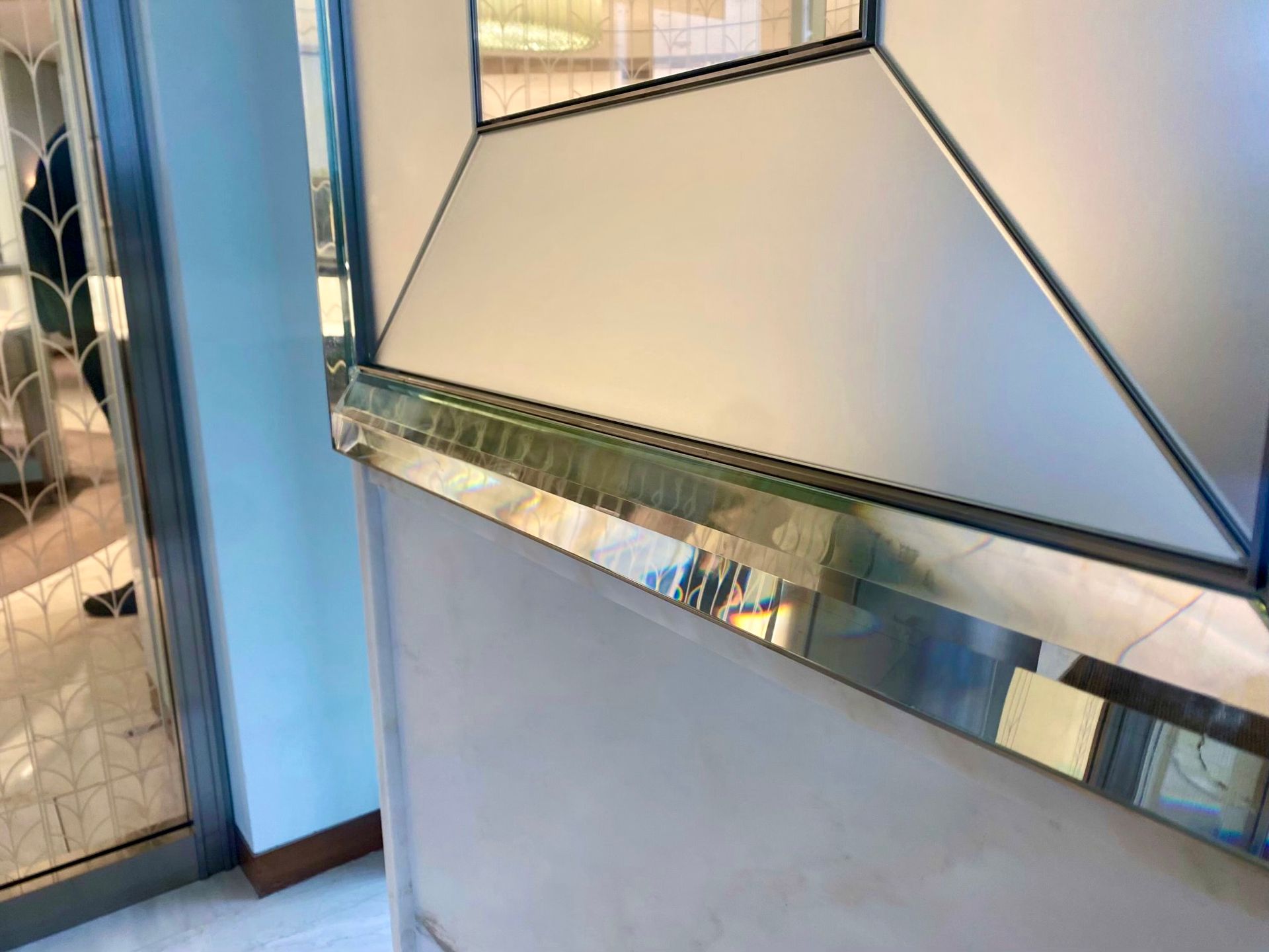 Close-up of a mirrored, geometric glass panel on a wall. Silver trim and frosted glass are visible.