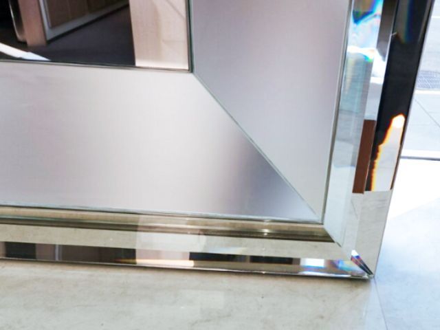 A mirror with a frame made of cast glass moulding sits on a tiled floor