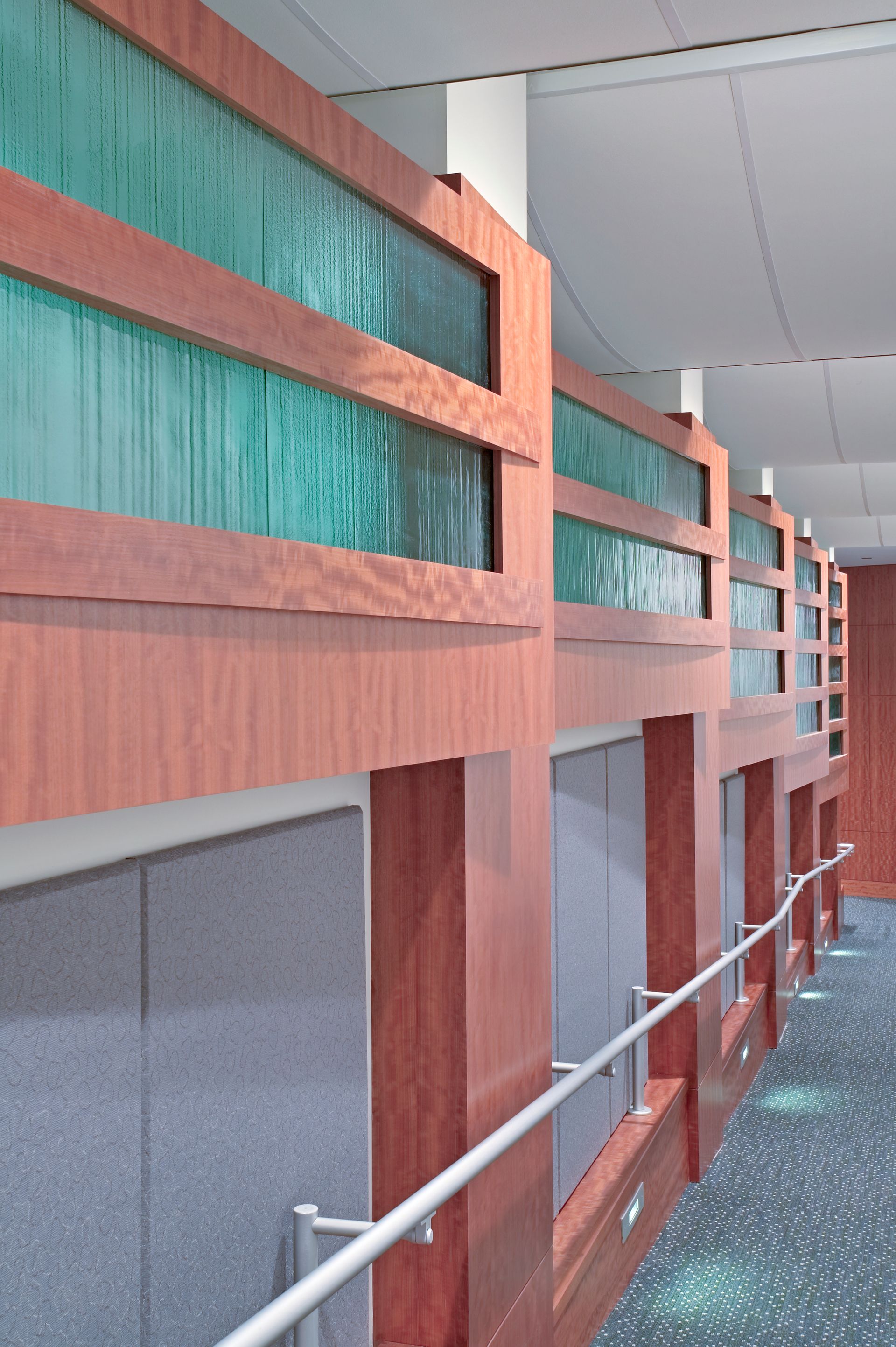 Indoor hallway with teal and coral wall panels, white railings, and a speckled floor.