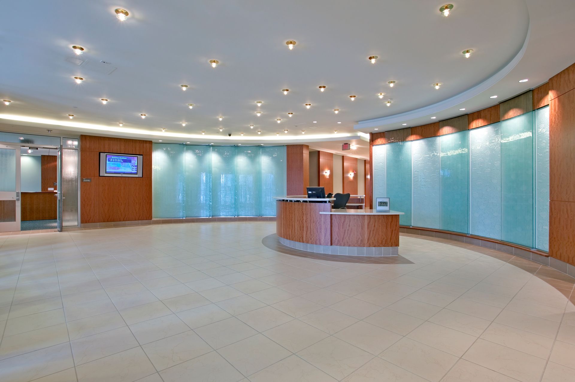 Empty modern lobby with curved desk, blue glass walls, and recessed ceiling lights