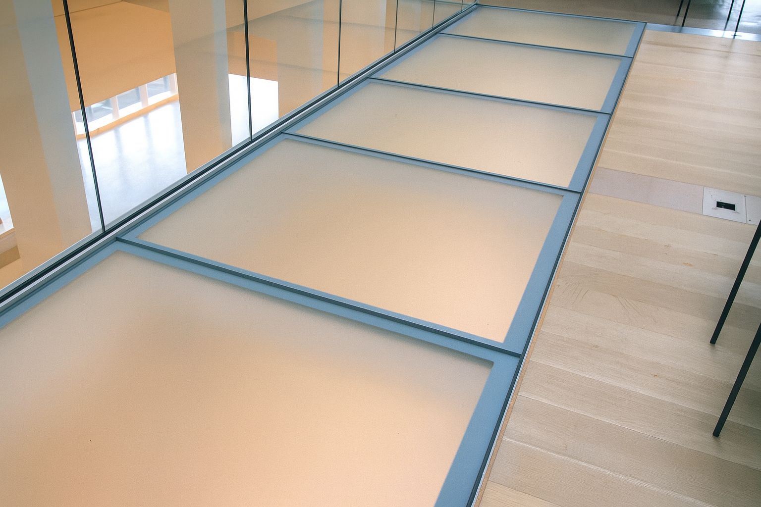 Glass walkway panels set in a blue frame on a wood floor, inside a modern building.