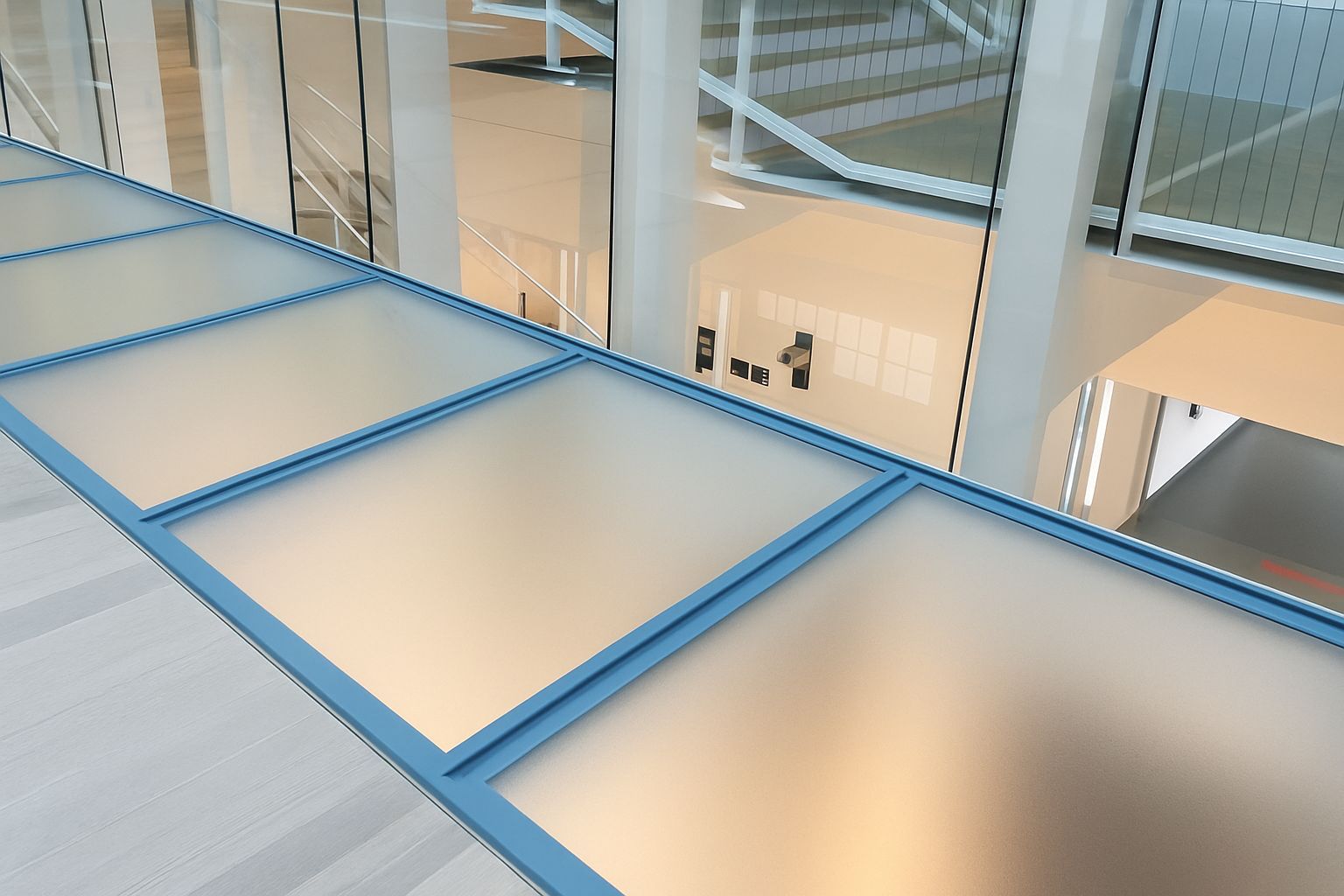 Glass walkway with blue trim overlooking a light-filled interior space.