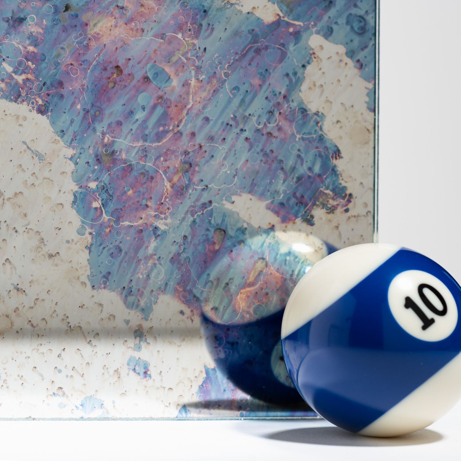 A blue and white number 10 billiard ball sitting in front of its reflection in an abstract, marbled-blue mirror.