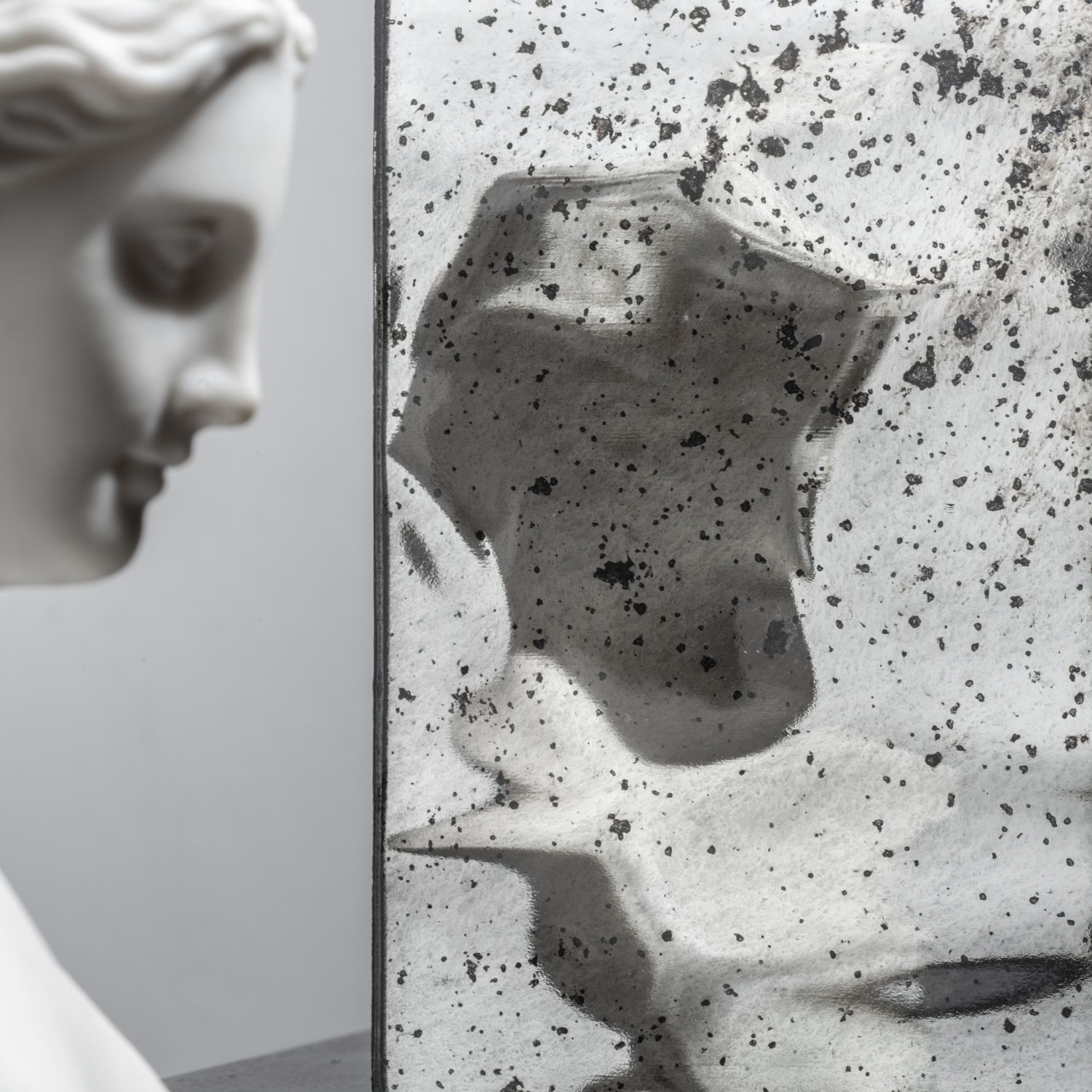 White marble bust beside a speckled translucent panel with abstract shadowy forms