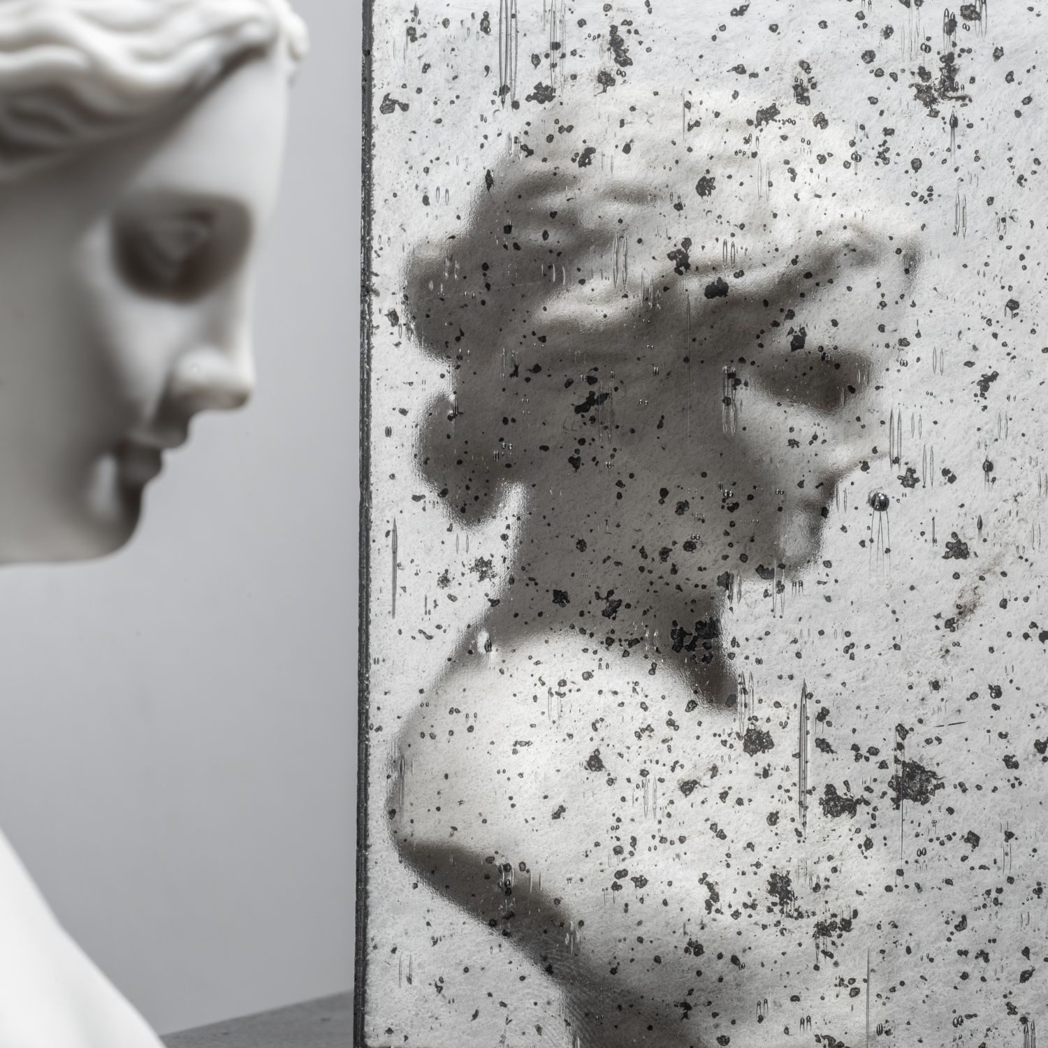 Close-up of a marble bust reflected in a cracked, speckled mirror or glass panel