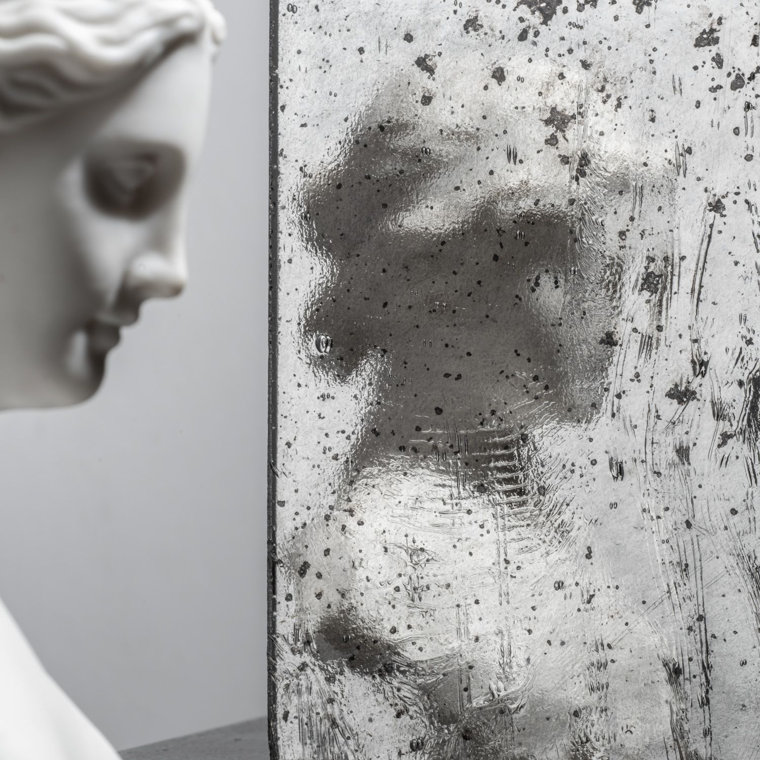 Gray bust beside a mirrored, speckled reflection creating a fragmented double portrait