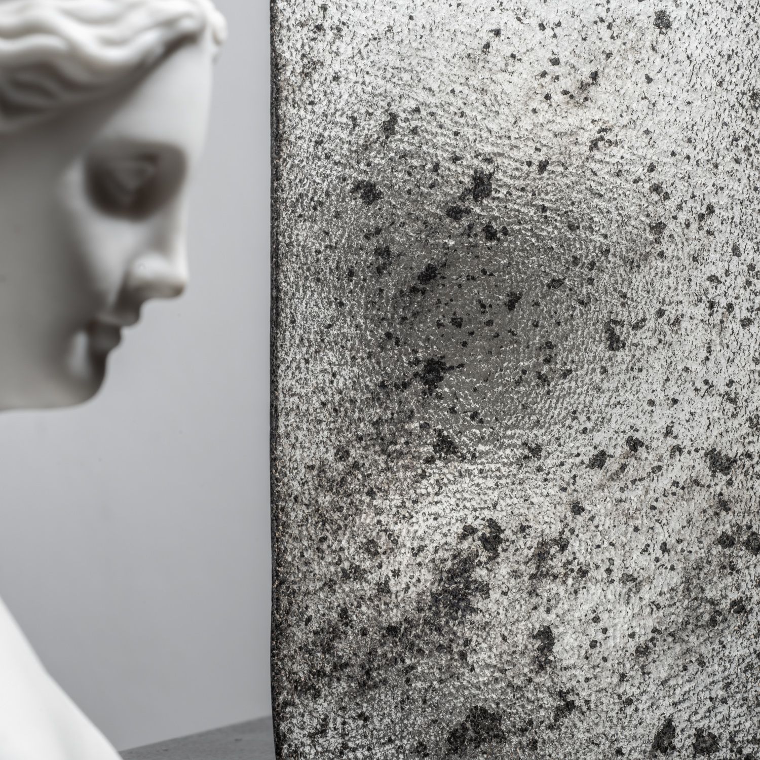 Marble bust beside a speckled gray abstract wall or panel