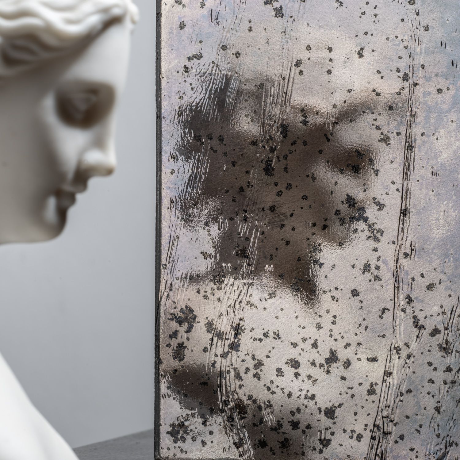 White classical bust beside a foggy glass panel speckled with dark spots