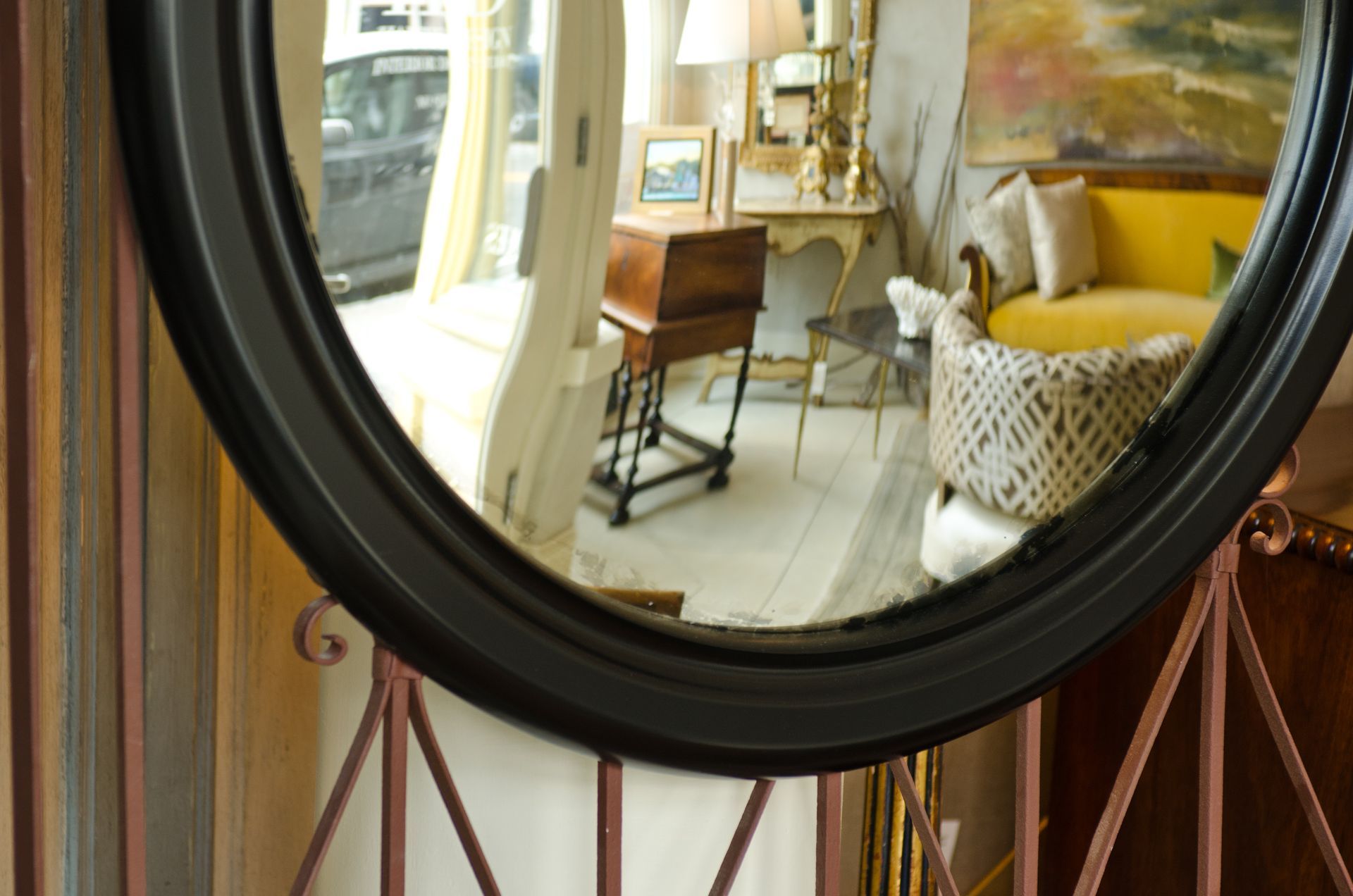 A round antique mirror shows a living room with a yellow couch
