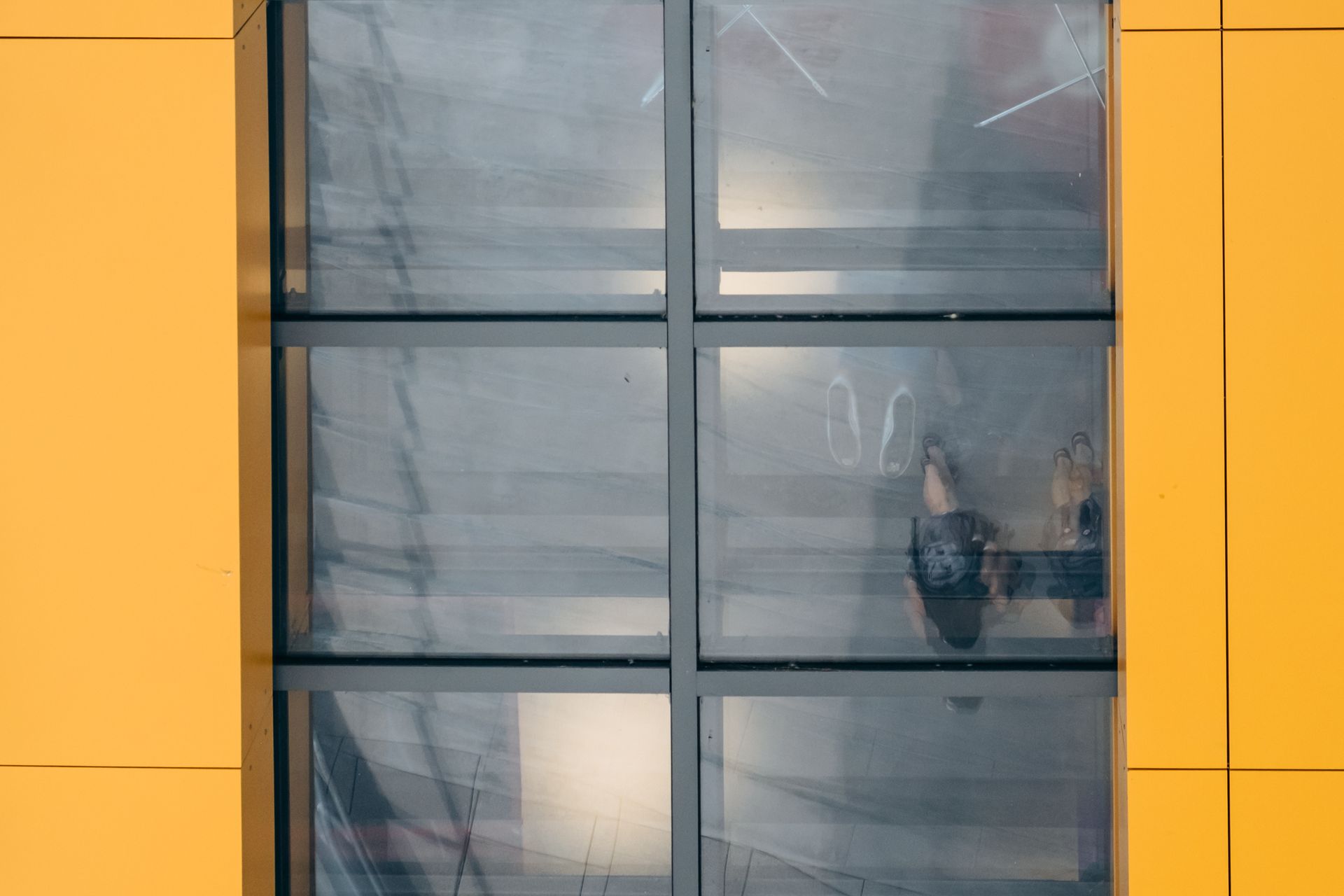 Yellow building facade with a six-pane window; a person's reflection visible.