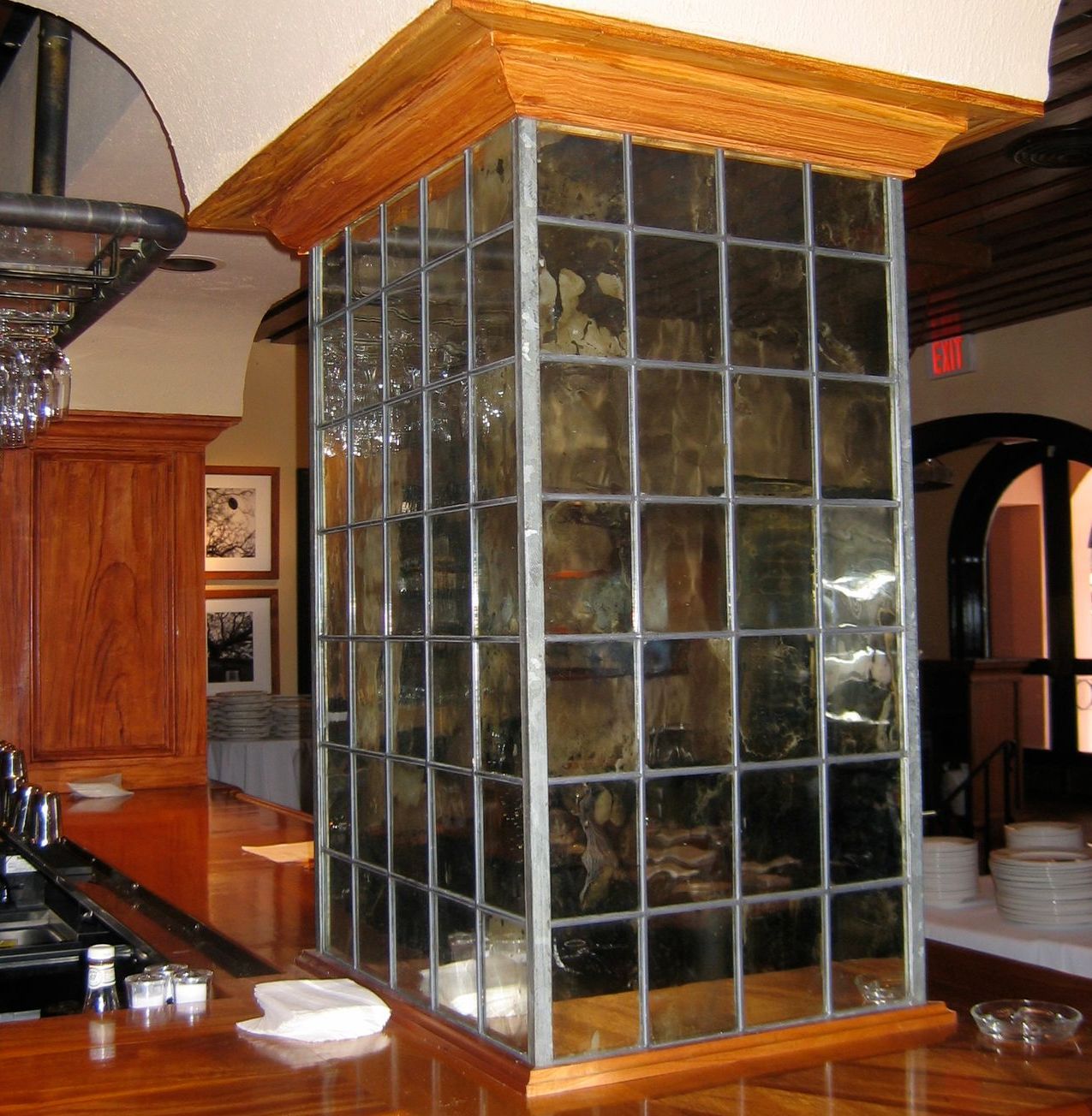 A mirrored glass bar column with a wooden top and base, inside a restaurant.