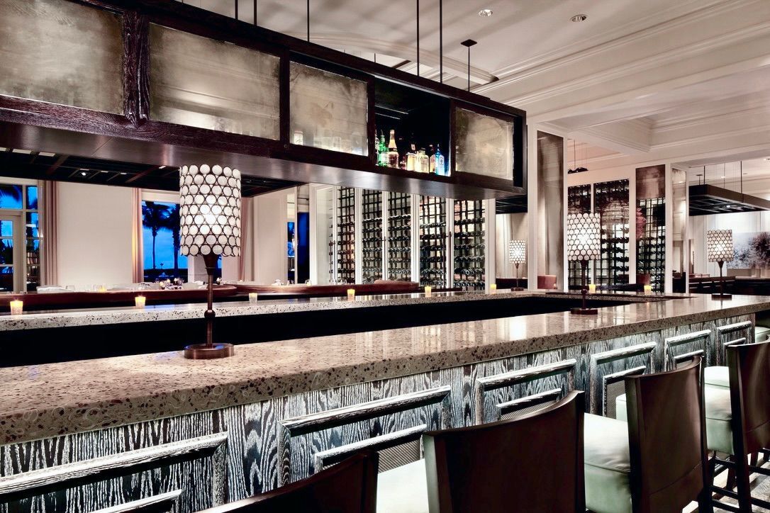 Elegant upscale bar with granite countertops, decorative lamps, a hanging antique mirror display, and rows of wine racks.