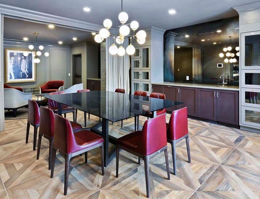 A dining room with a black table, red chairs, and a large light fixture. Wooden floor and cabinetry.