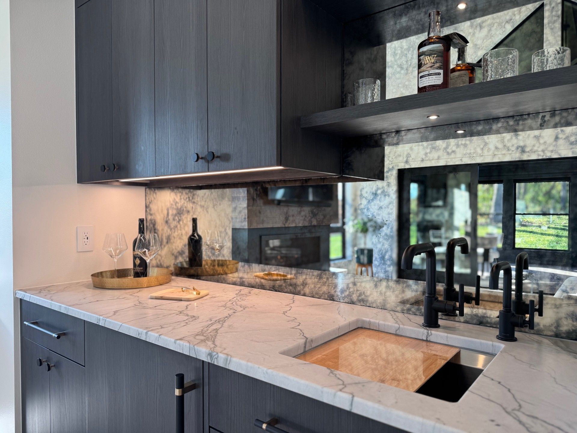 Dark wood kitchen with marble countertop and antique mirrored backsplash, drinks on shelf.