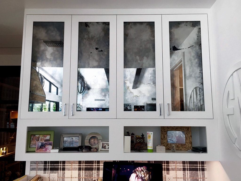 White cabinet with mirrored doors over a shelf displaying framed photos, lotion, and TV.