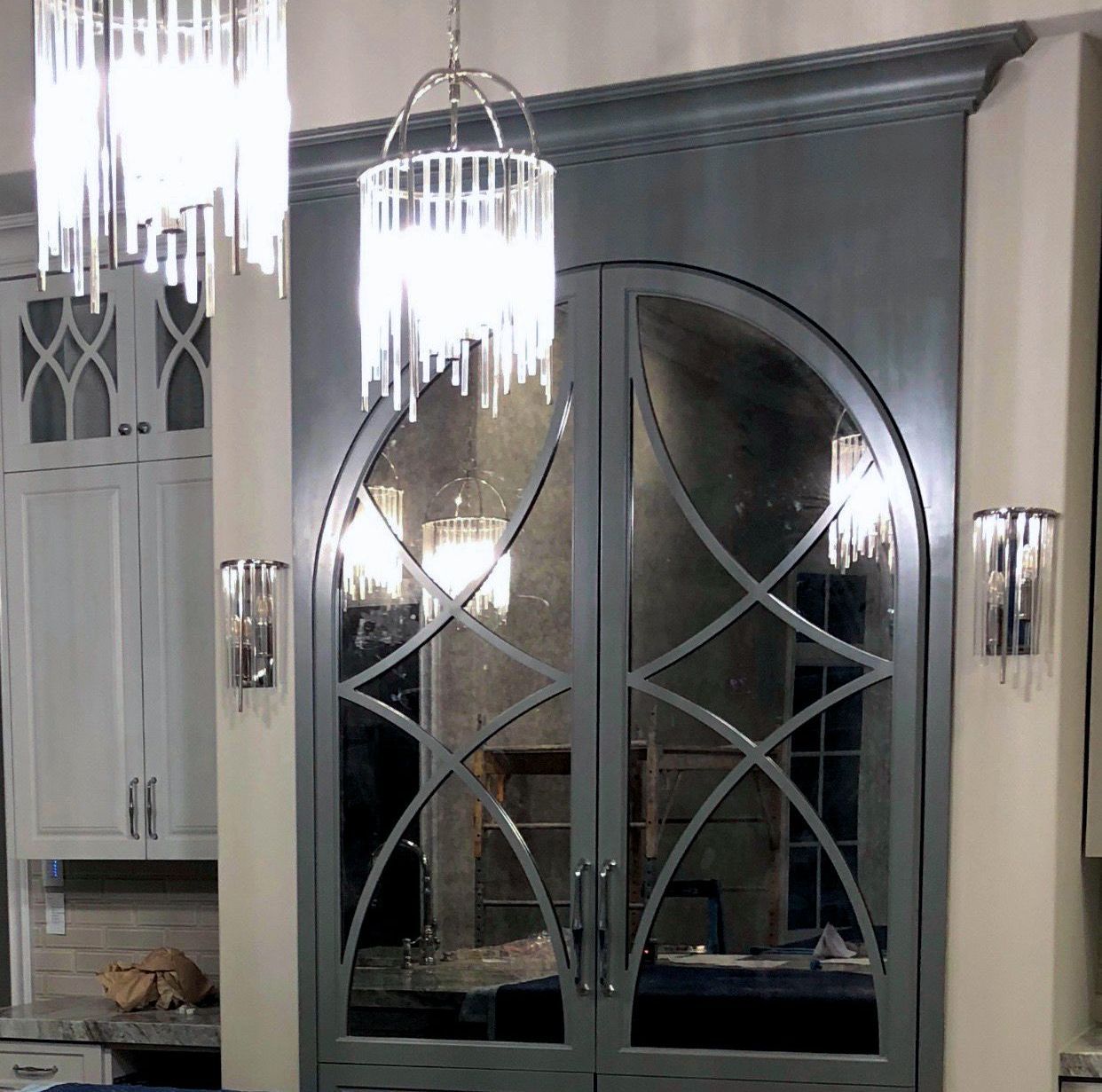 A gray cabinet with a antique mirrored door and a chandelier hanging from the ceiling