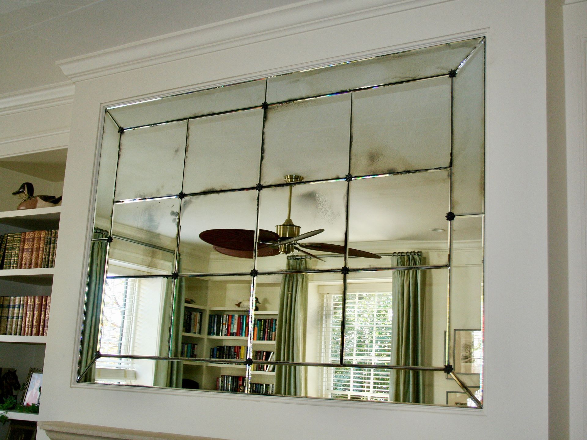 A ceiling fan is reflected in a large antique mirror in a living room