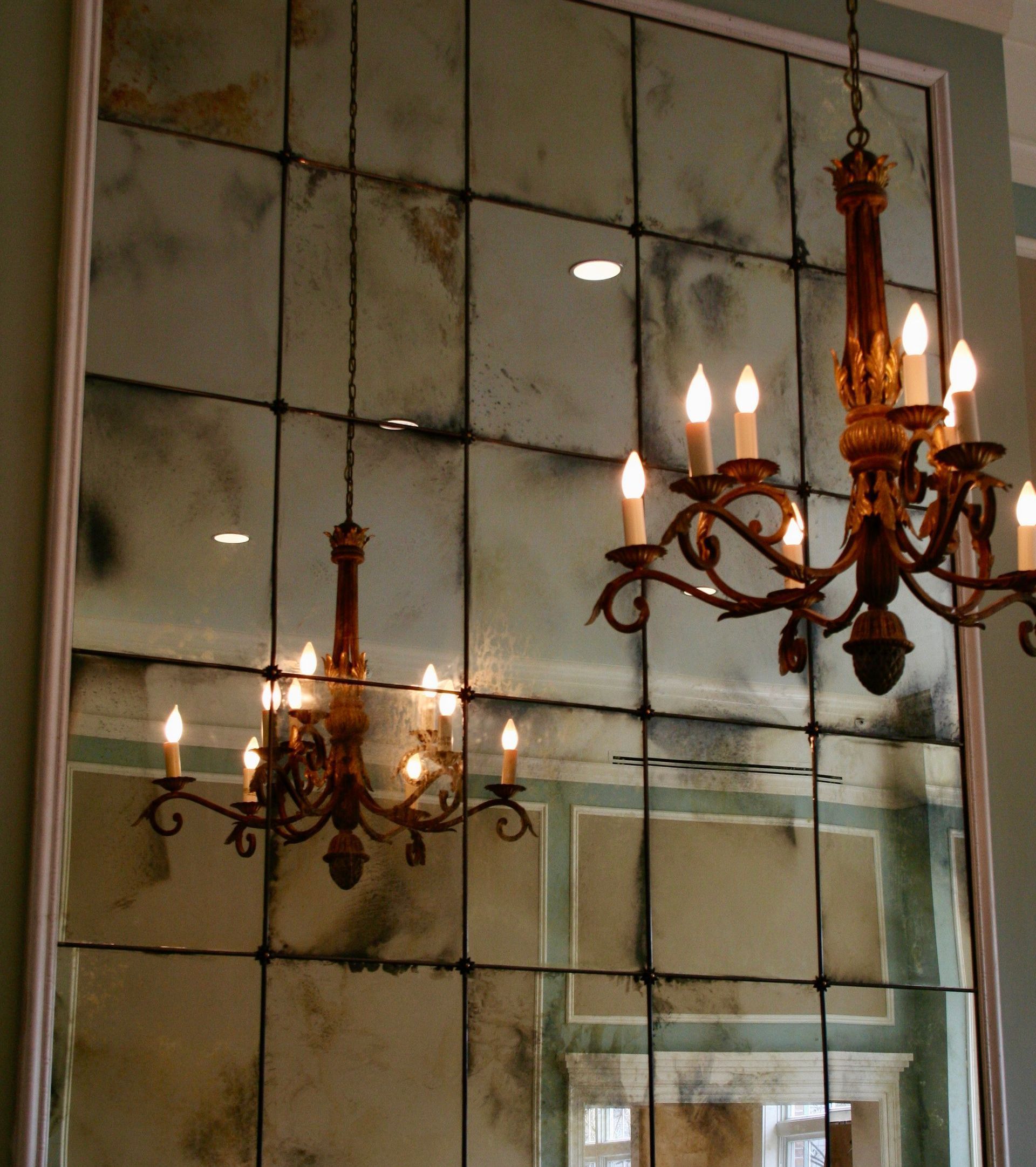 Large paneled mirror with aged finish, reflecting two candle chandeliers in a room with mint-green walls.