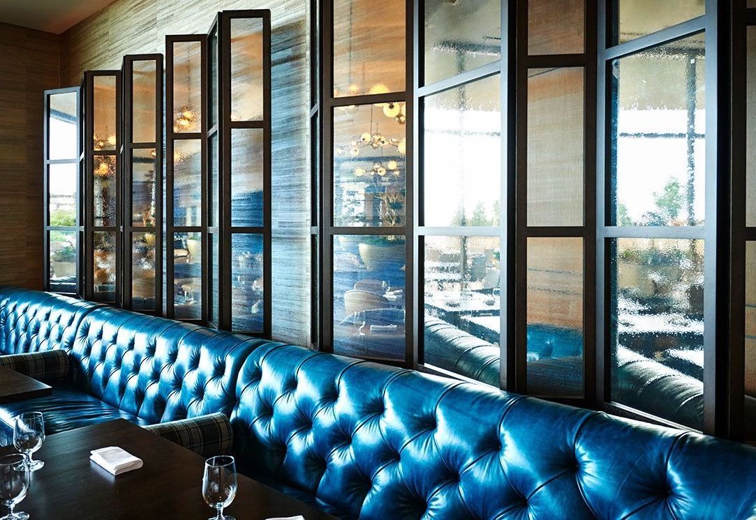 A blue leather couch is sitting in front of a wall of windows in a restaurant.