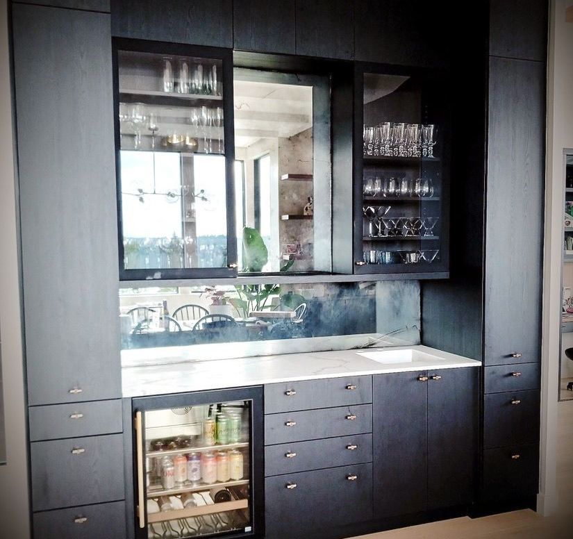 A kitchen with black cabinets and a wine cooler backed by antique mirrors