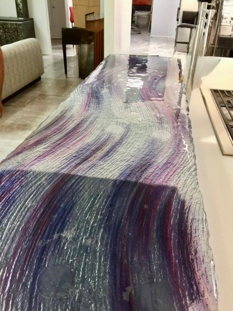 Long, glass-topped bar with flowing purple and white design, in a room with a white sofa and open doorway.