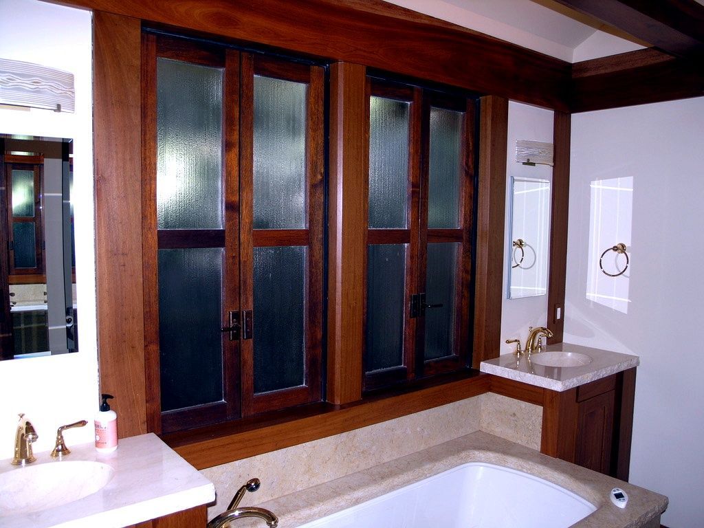 Bathroom with wood-framed frosted windows, double sink vanity, and a large bathtub underneath.