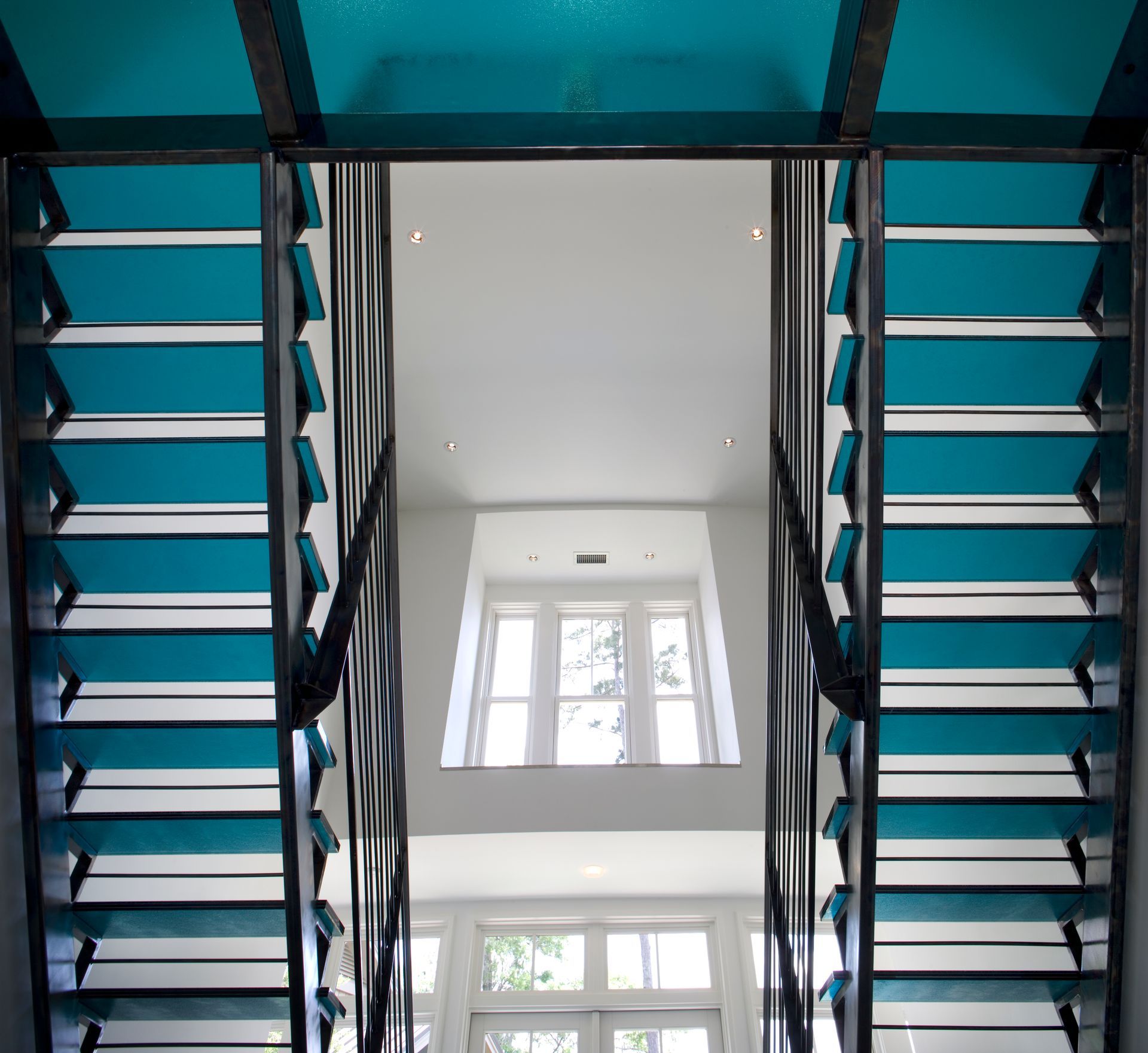 Blue and white interior stairway.  Geometric design, large windows at end of hall.