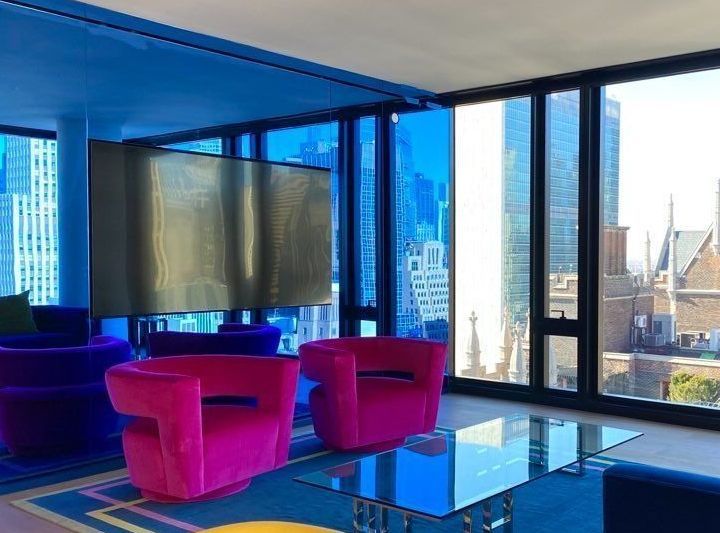 Brightly colored lounge with pink chairs, blue accents, and a city view through windows.