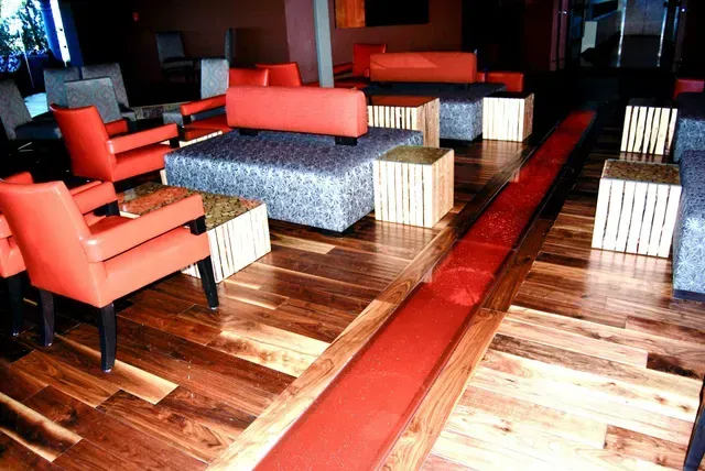Lounge with orange chairs, grey sofa, wooden tables, and a long red floor feature on a polished wood floor.