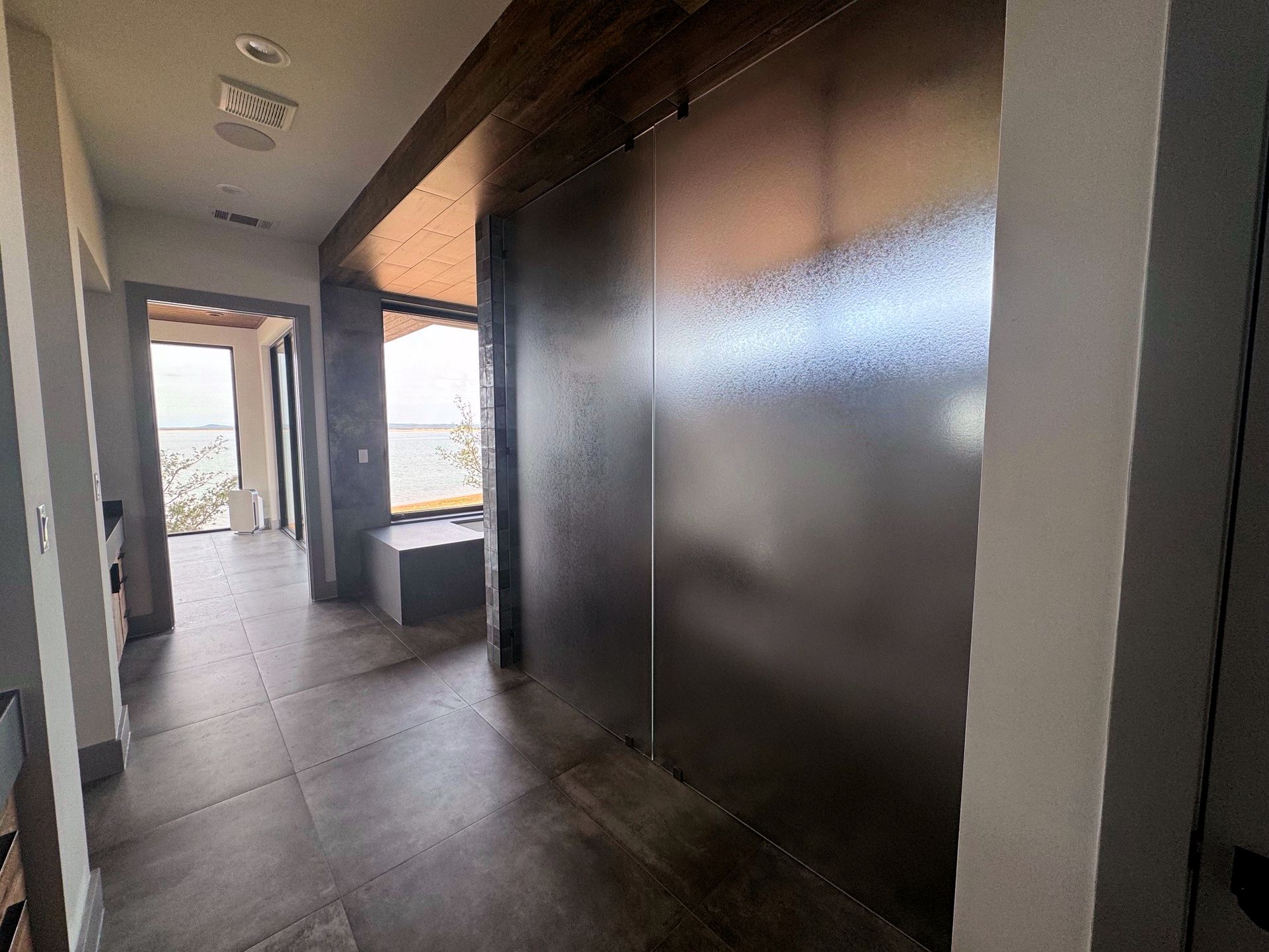 Hallway with dark flooring, metallic wall paneling, and an open doorway to a windowed area.