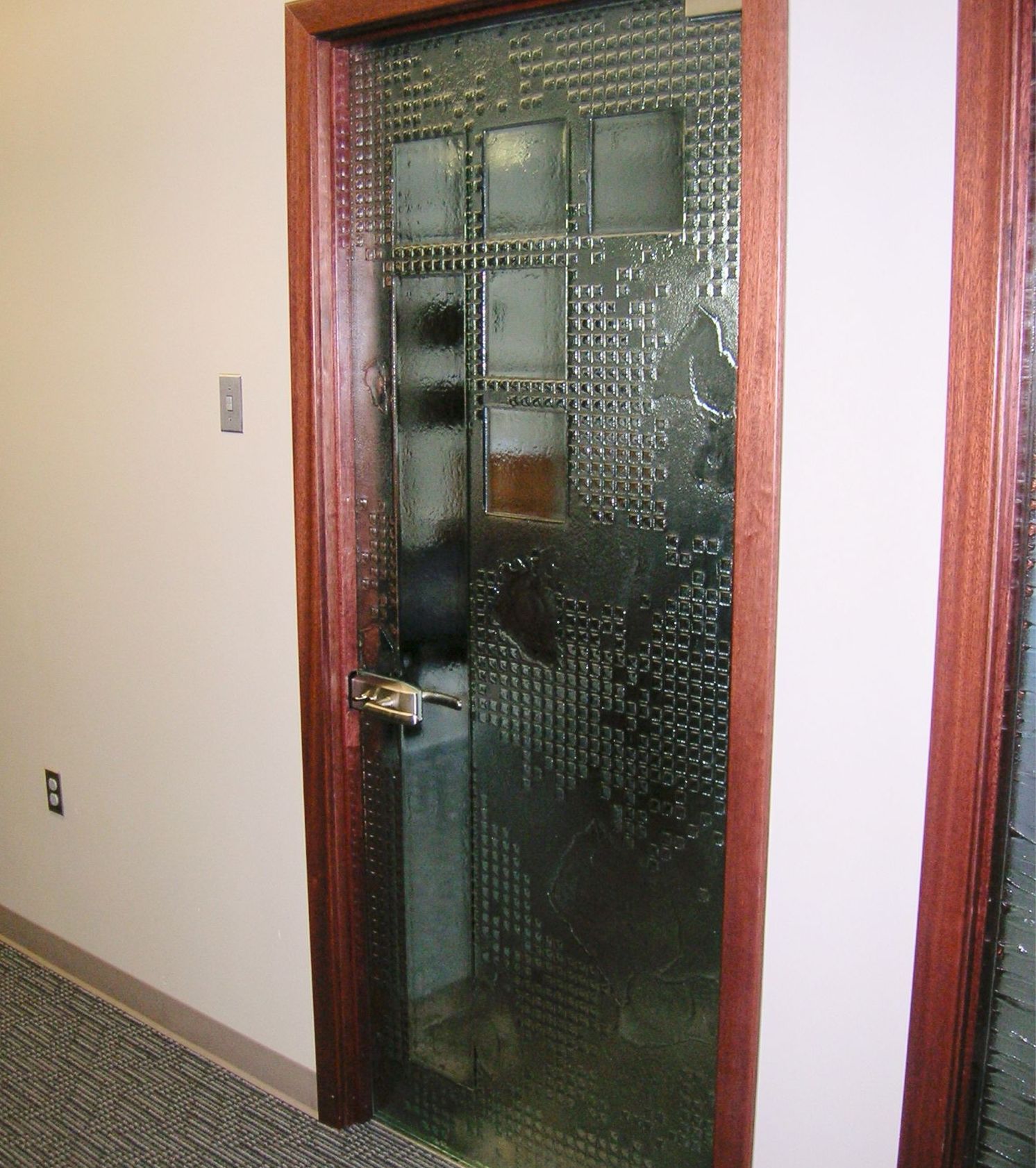 Glass door with a textured pattern and brown wooden frame, leading to a room with a computer.
