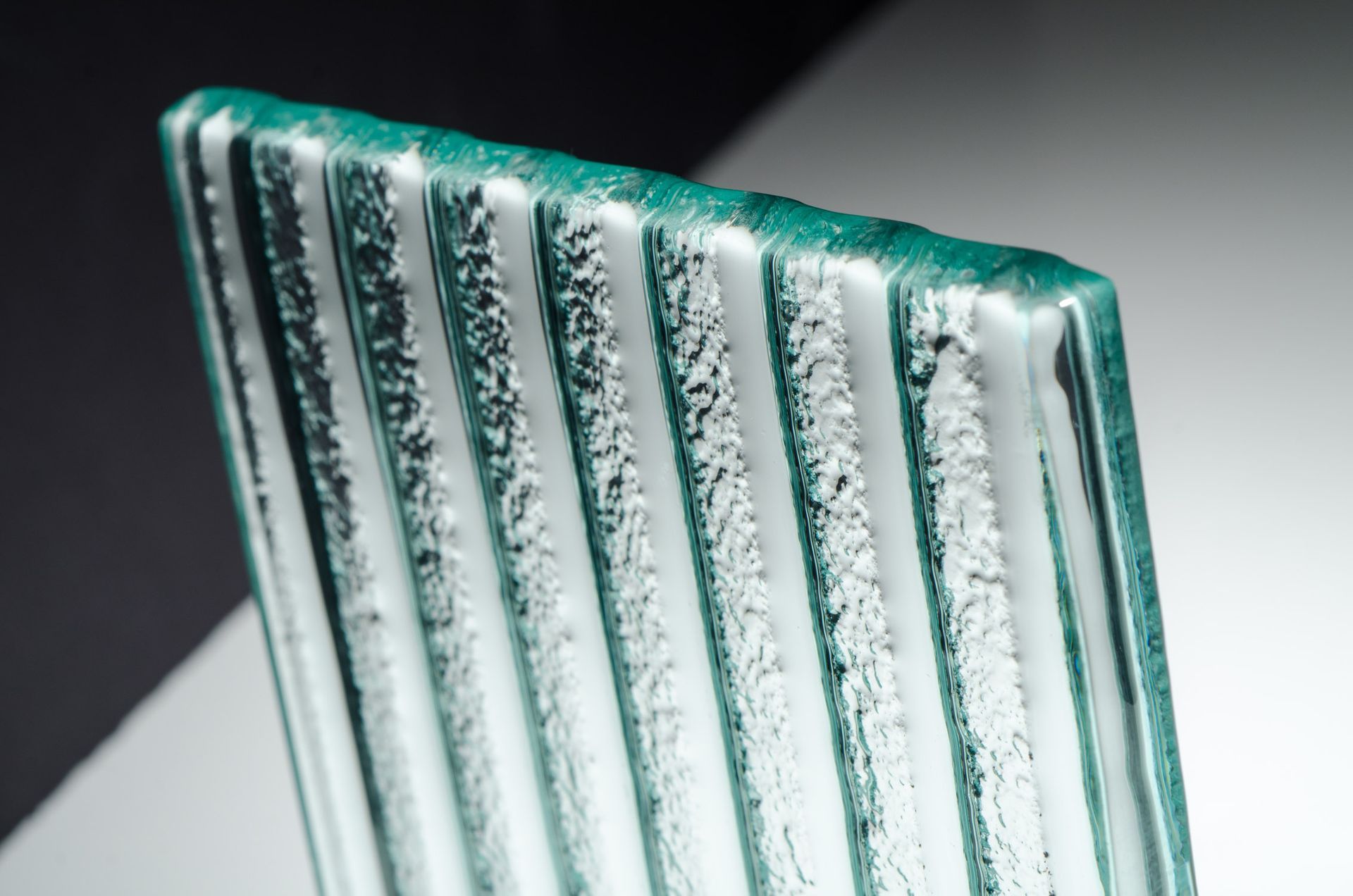 Close-up of textured, ribbed glass edge, showing the rippled surface in shades of green.