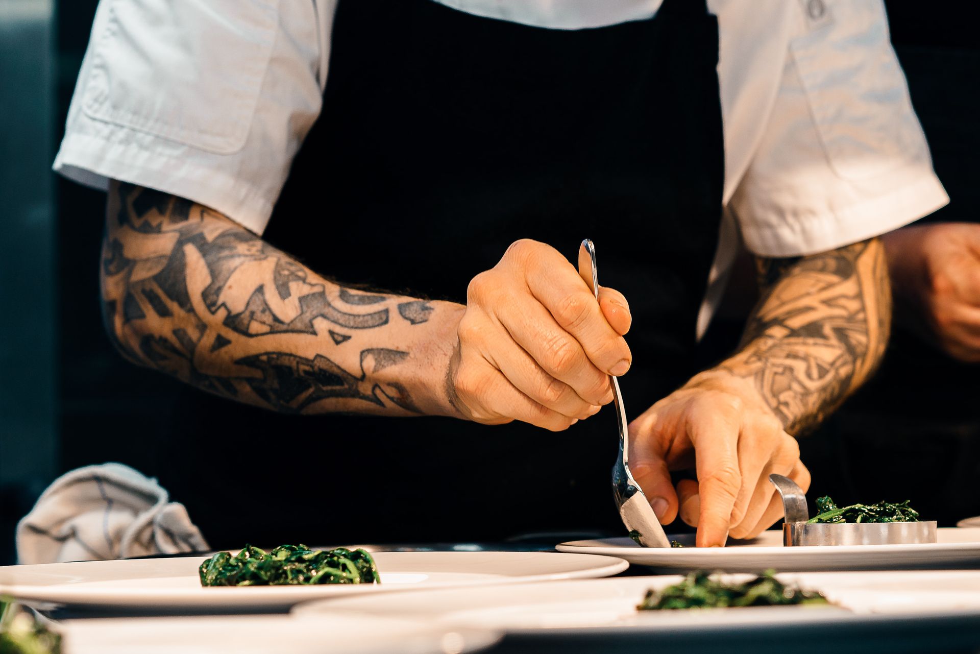 A chef plating greens on white plates