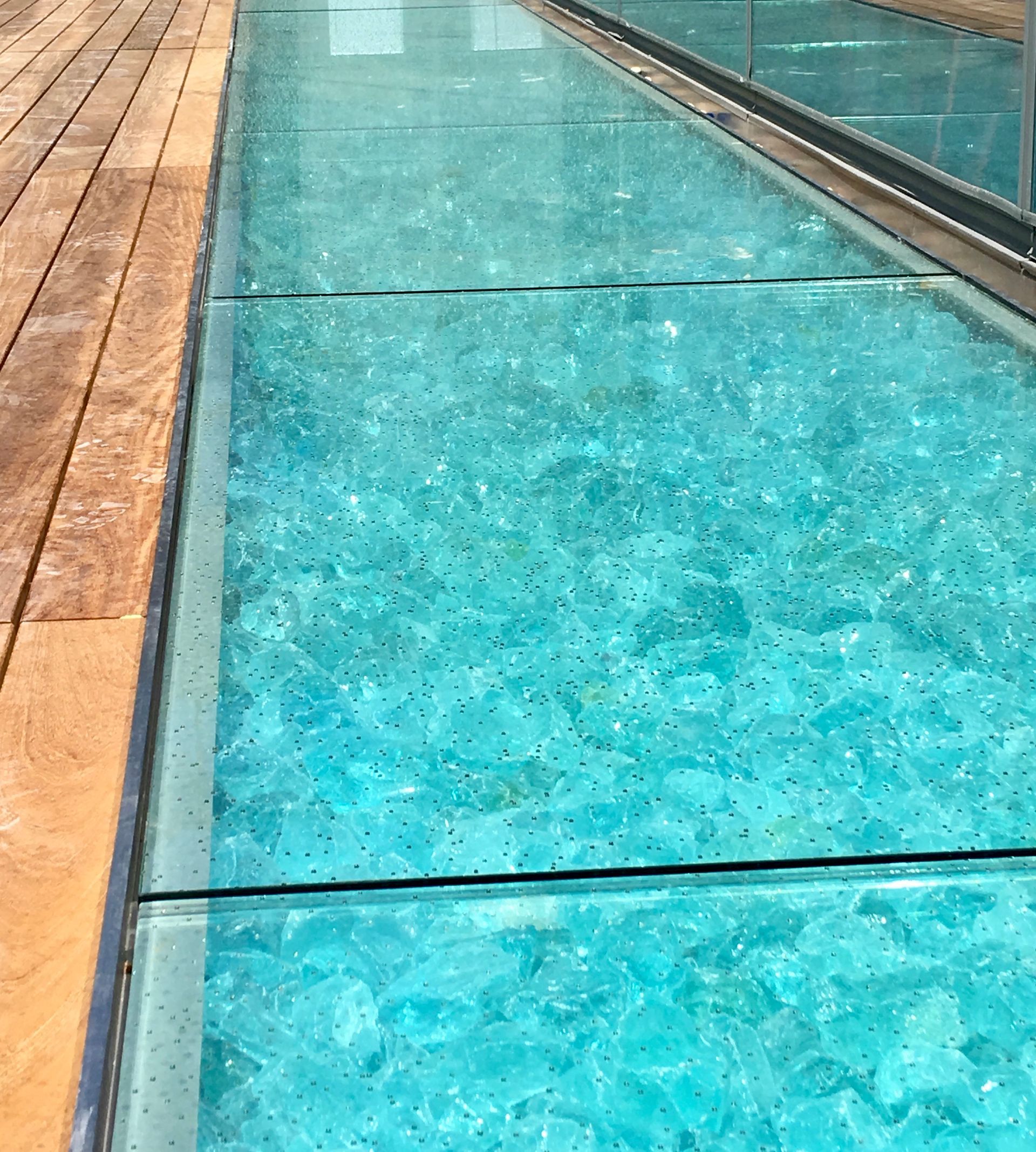 Glass-bottomed walkway filled with turquoise glass pieces. Wooden deck to the left.