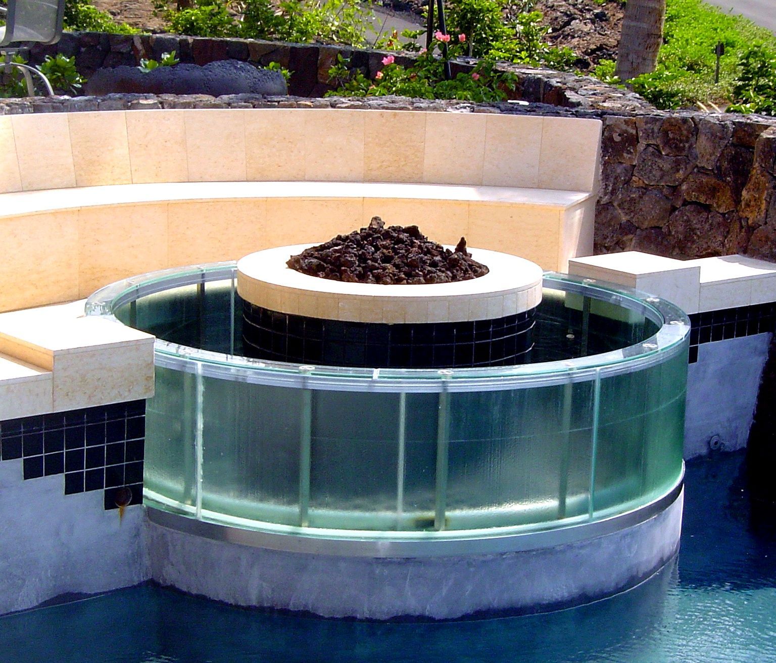 Modern circular fountain with a glass basin and stone planter in a landscaped garden